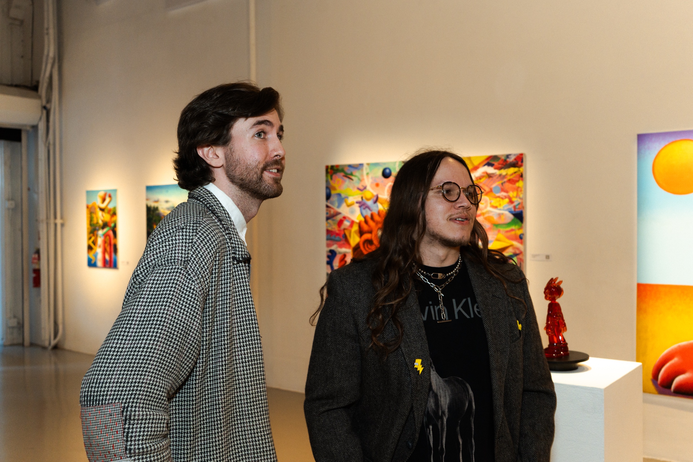 Two guests talk in the gallery with paintings and a red sculpture on a plinth behind them