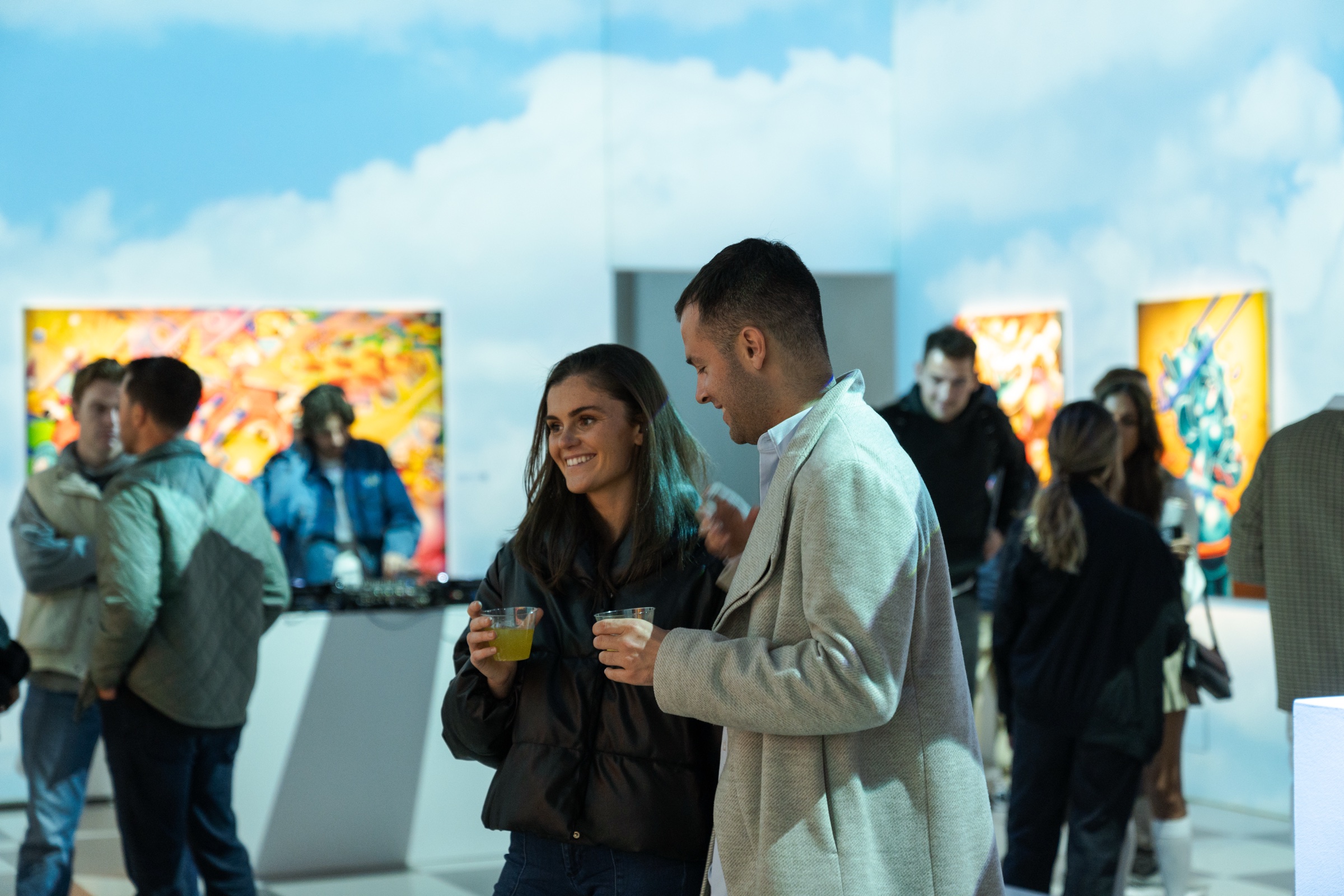 A couple hold drinks in the sky projection room as other guests view canvases behind them