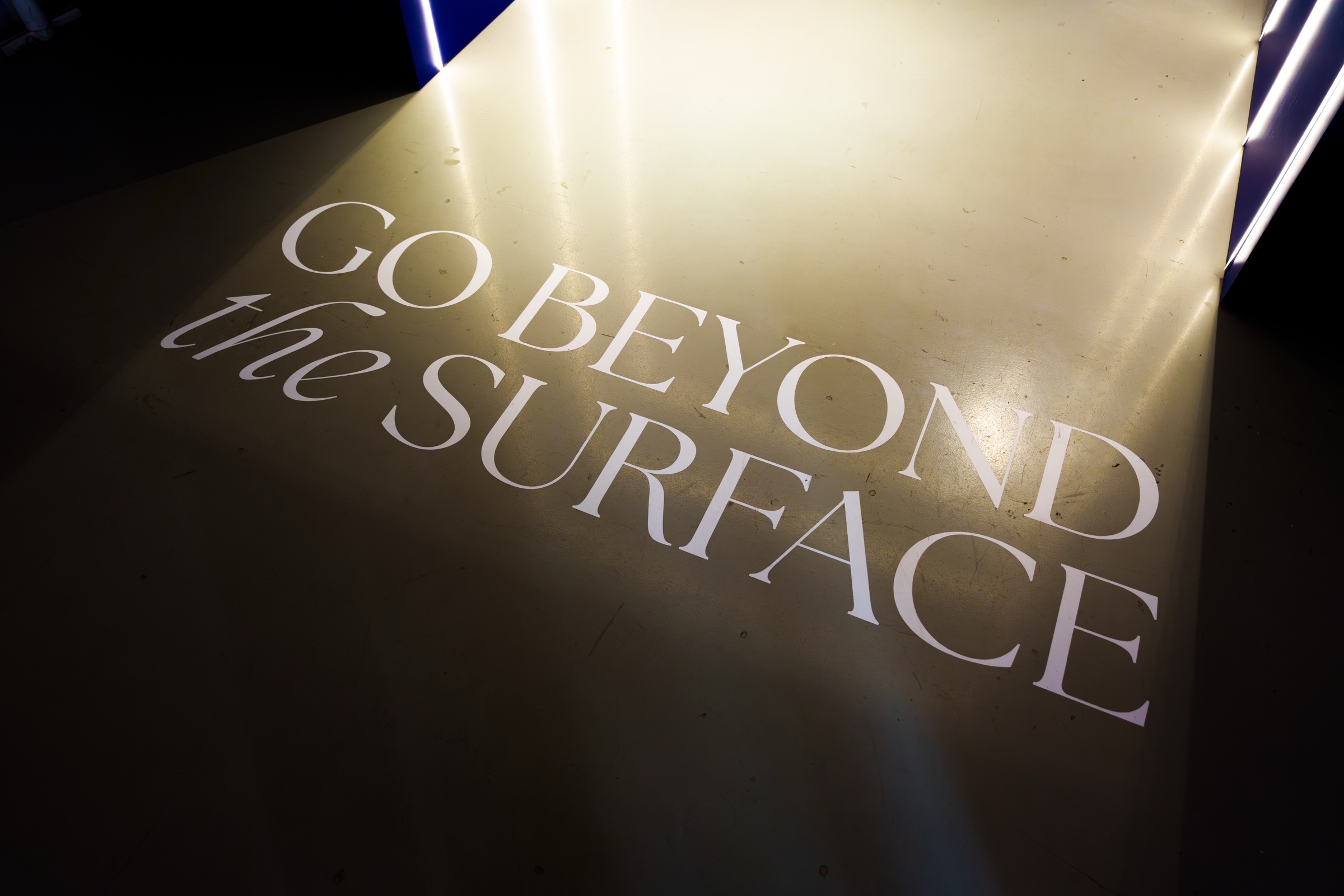 The words Go Beyond the Surface printed on a floor lit by a warm spotlight