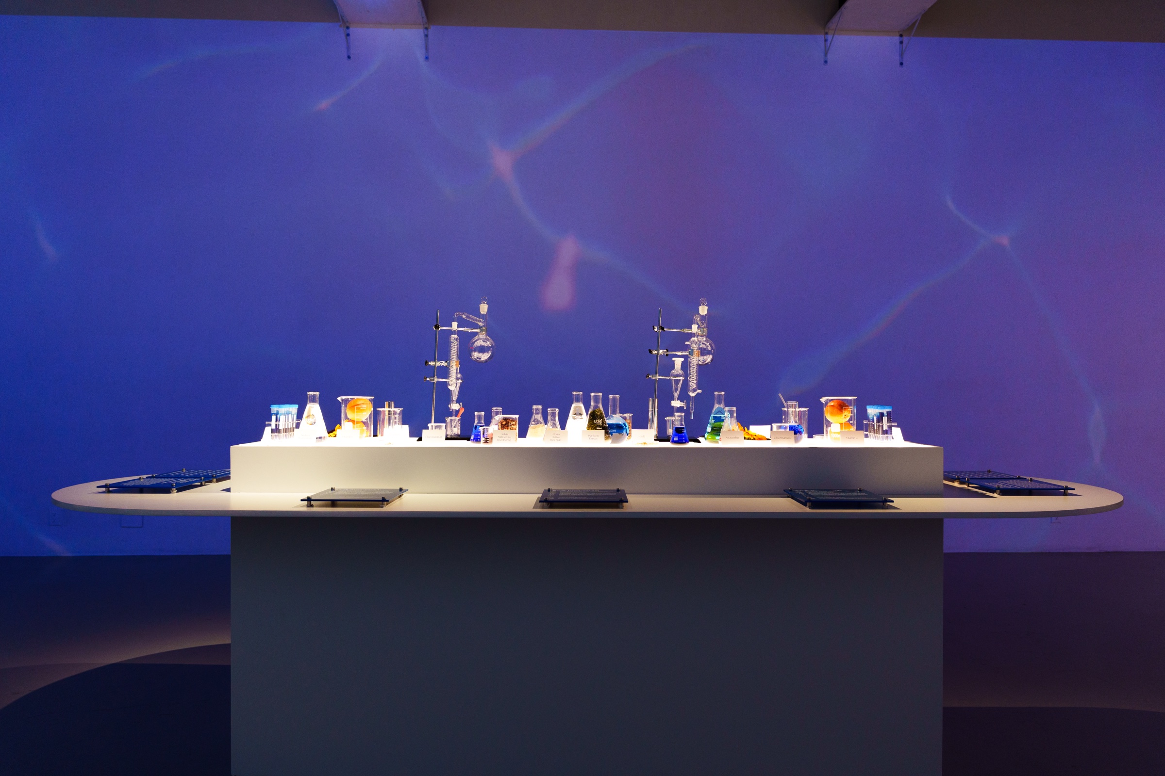 Glass laboratory flasks and beakers glowing on a white counter against a deep blue projected wall