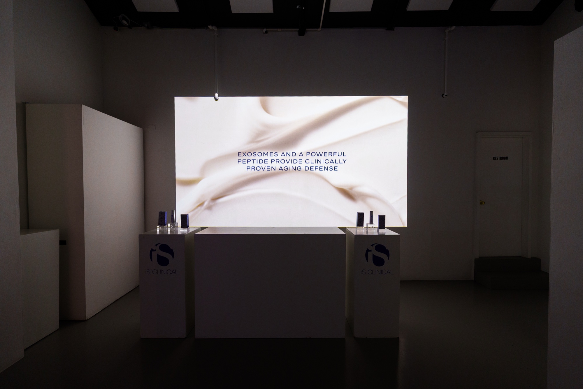 Two white plinths with serum bottles below a cream toned screen reading Exosomes and a powerful peptide