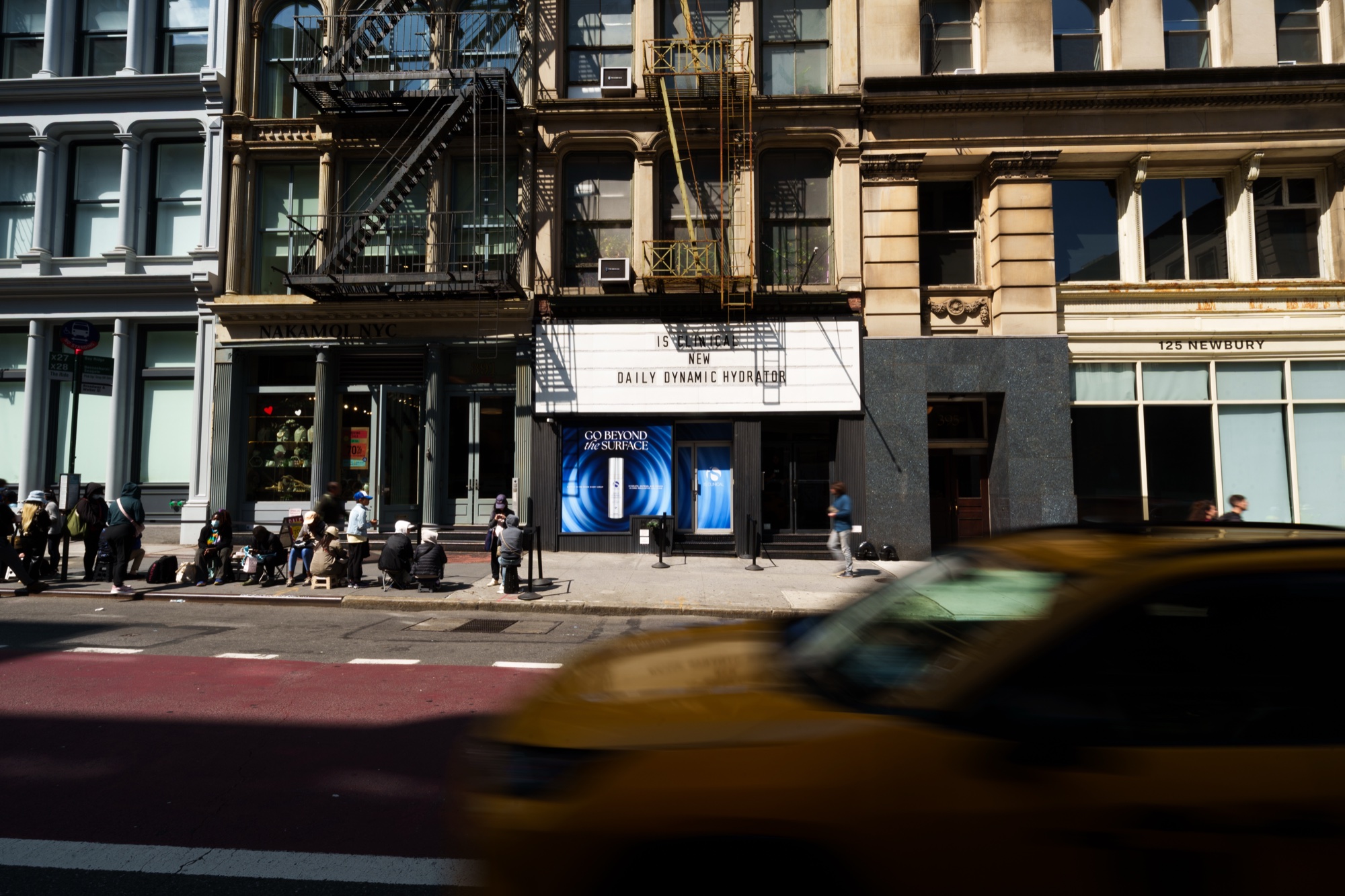 Storefront marquee advertising Daily Dynamic Hydration on a sunny street as a yellow taxi blurs past