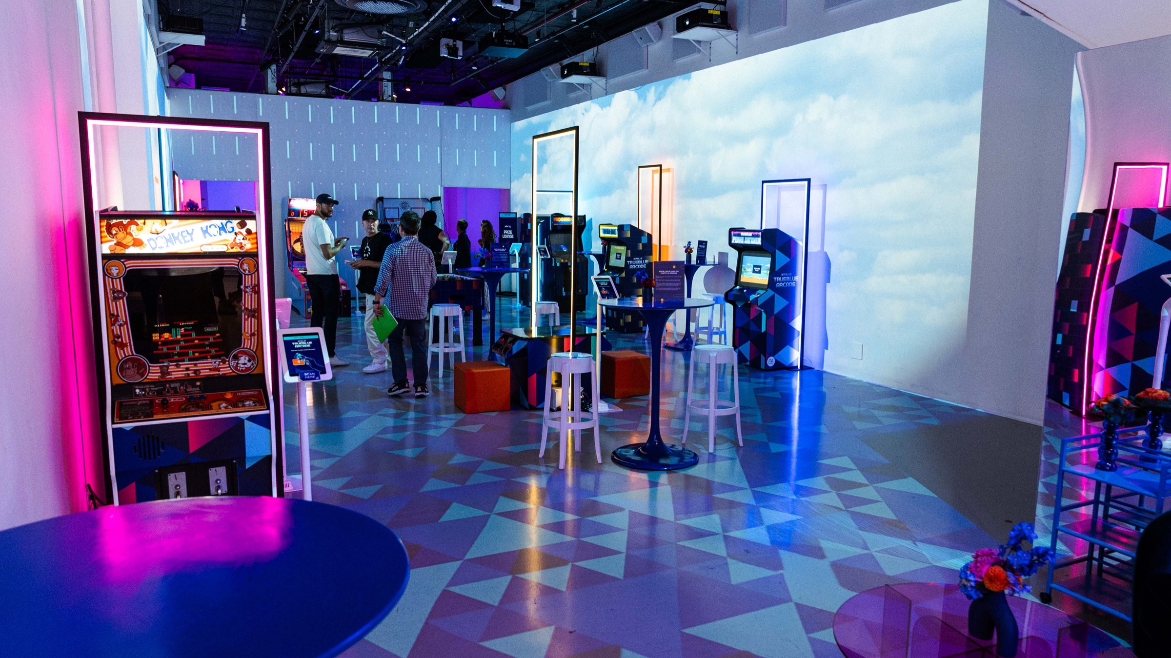 Wide view of the JetBlue arcade with glowing orange doorways, cloud walls and a geometric blue floor