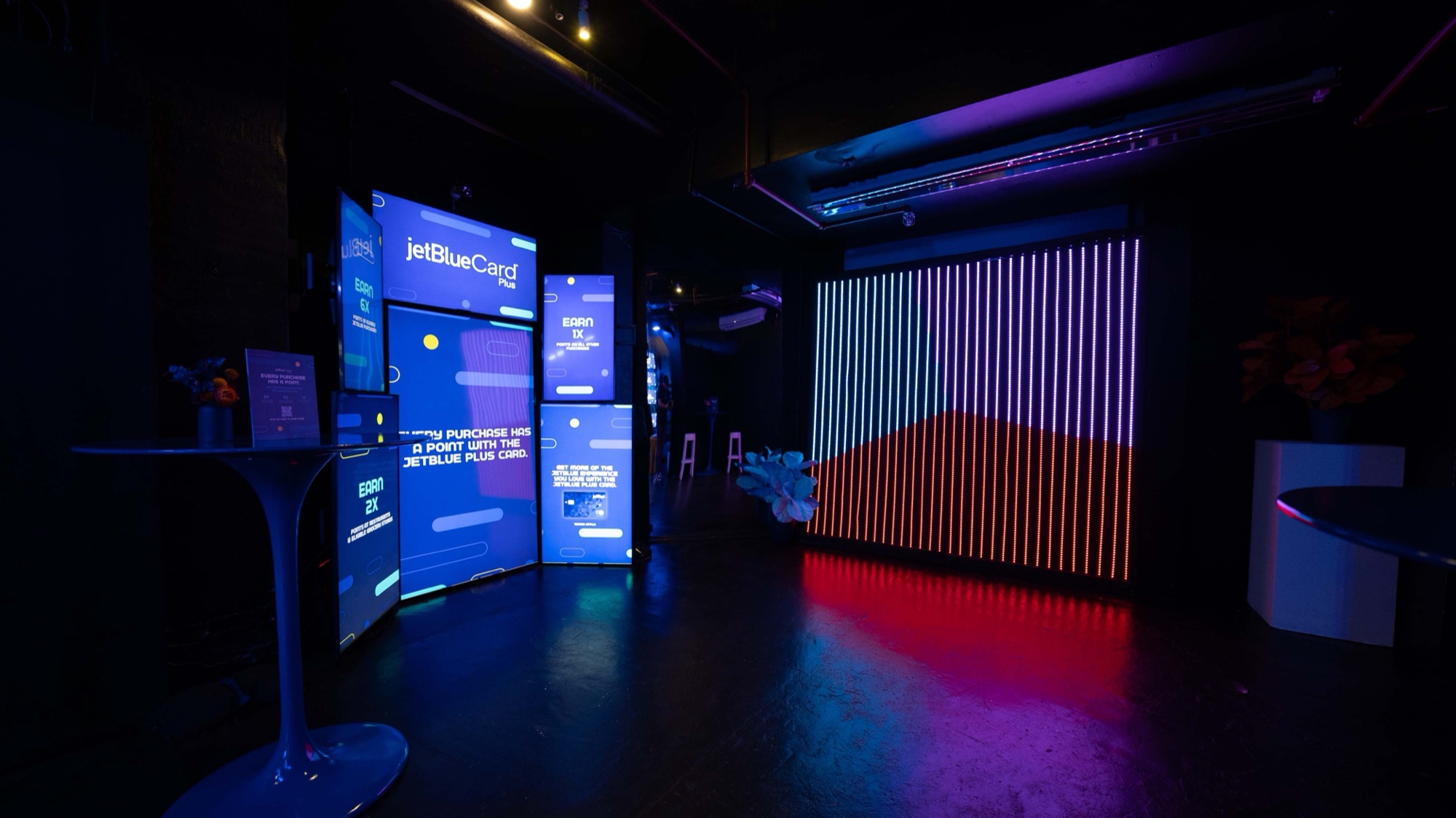 TrueBlue Ultimate Packer arcade cabinet glowing against a wall covered in cloud projections at the JetBlue arcade