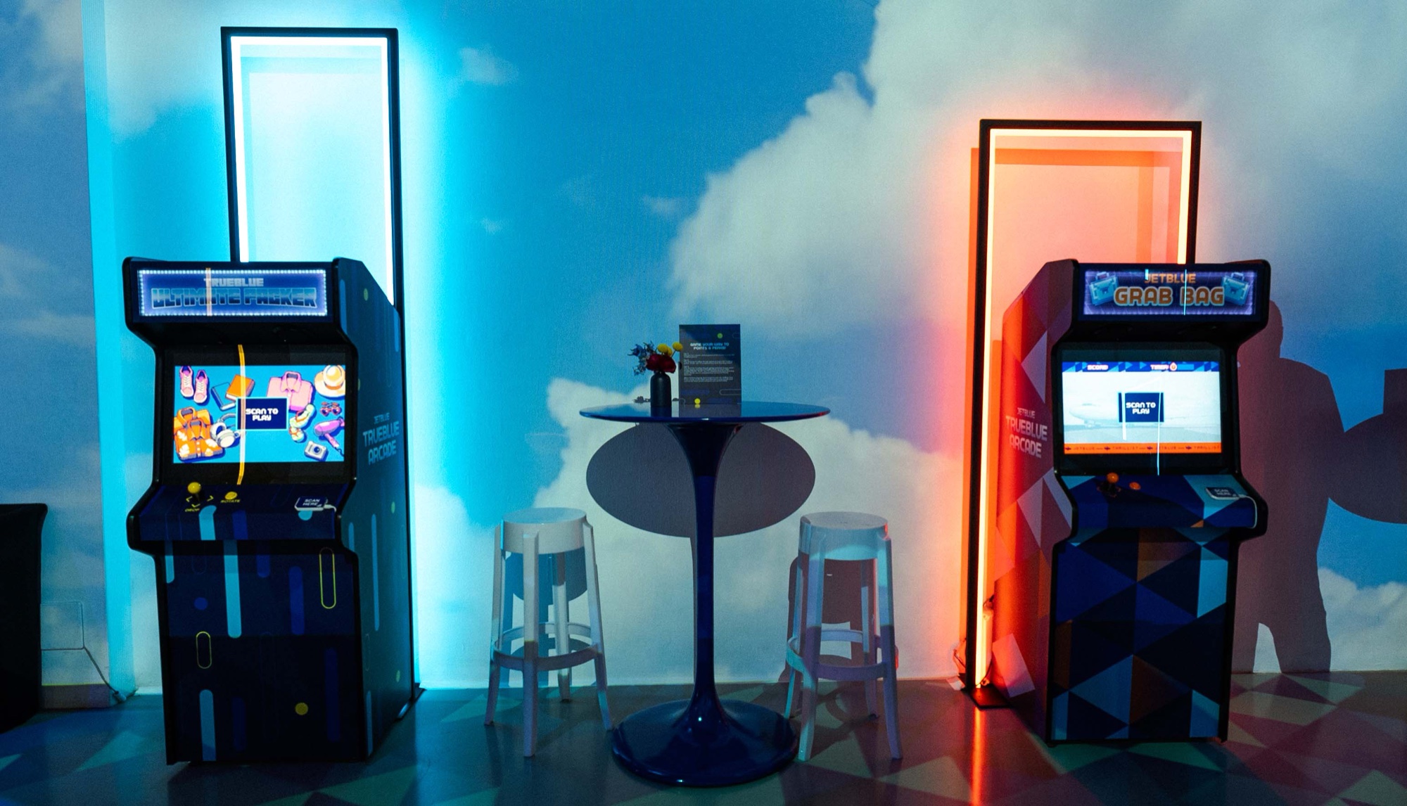 Guest leans into a JetBlue TrueBlue Arcade cabinet while friends chat nearby in blue light