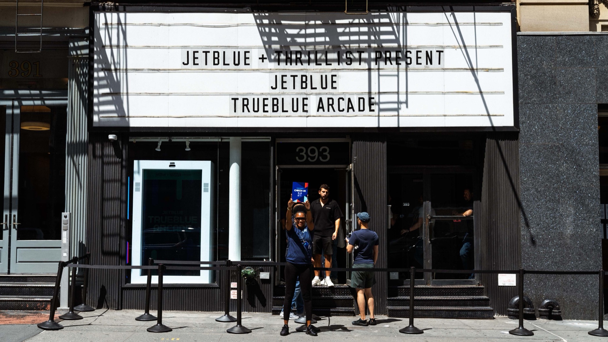 A theatre marquee reads JetBlue TrueBlue Arcade above a black storefront with guests waiting on the sidewalk