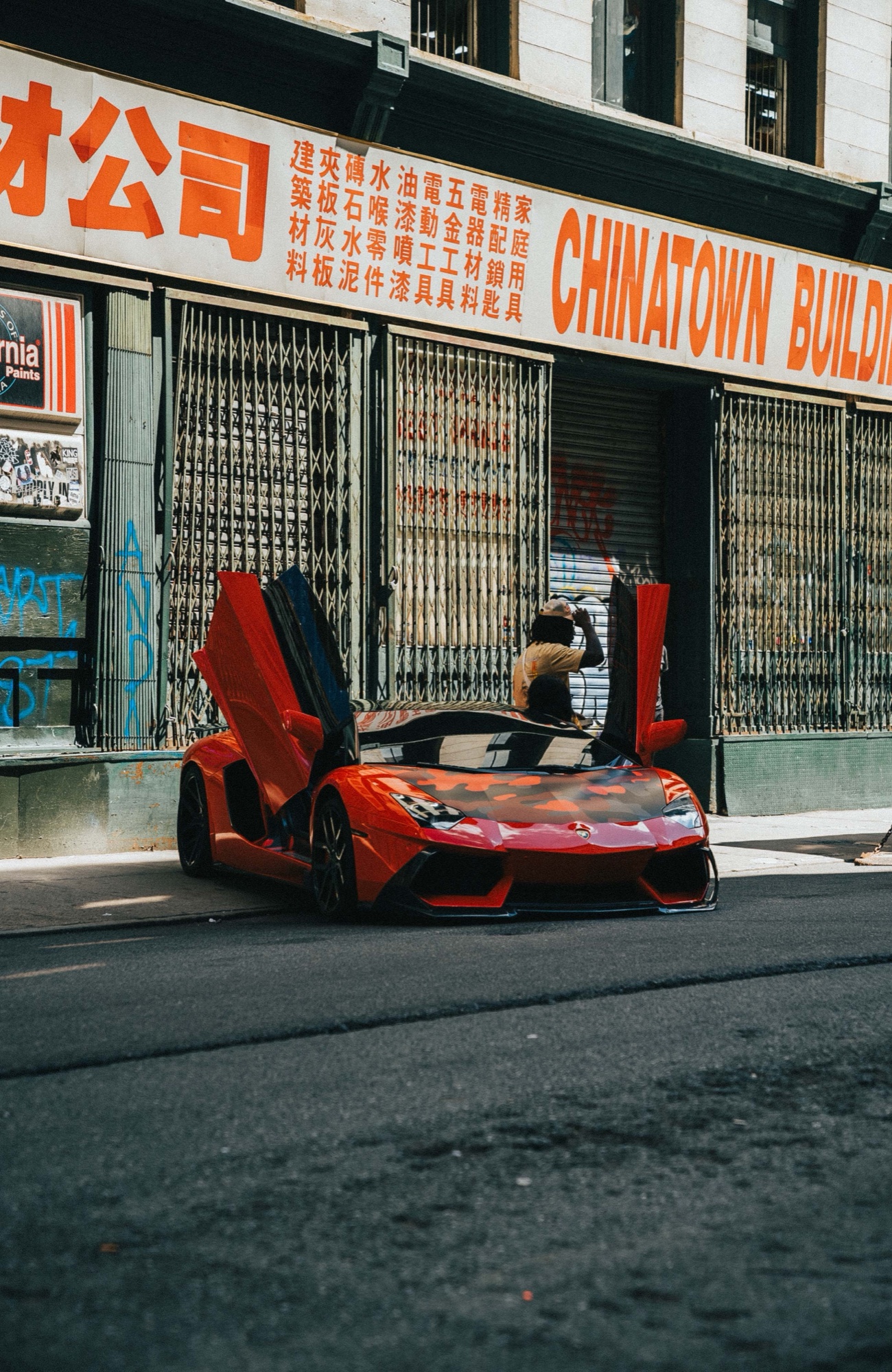 A red sports car with scissor doors raised parked below an orange Chinatown building sign, a person leaning in