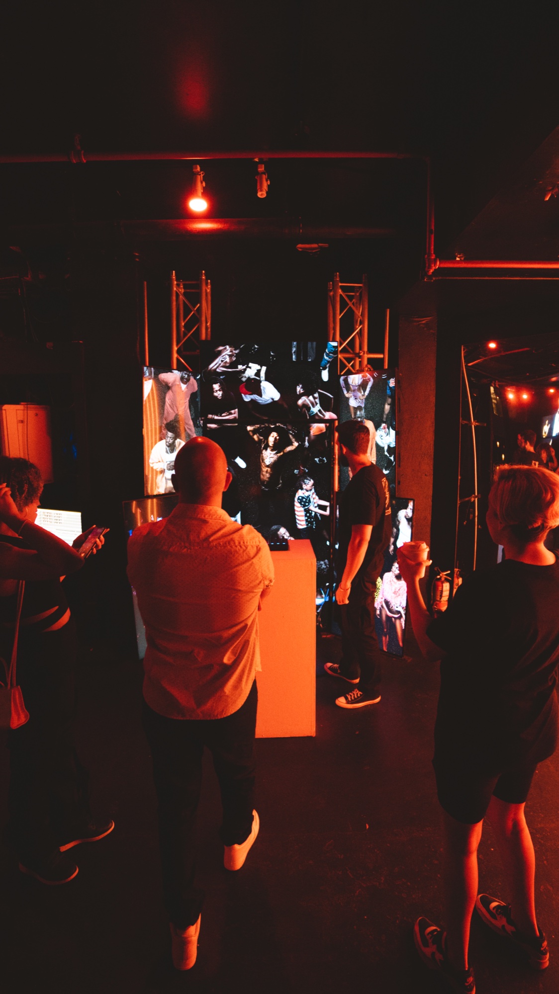 Guests under red light watch a tall video screen framed by metal truss towers