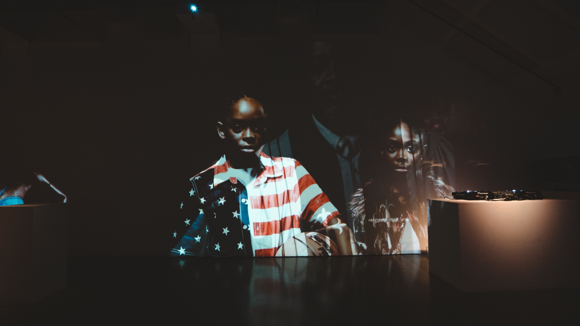 Projected portrait of a man in a stars and stripes shirt beside a woman above a DJ plinth