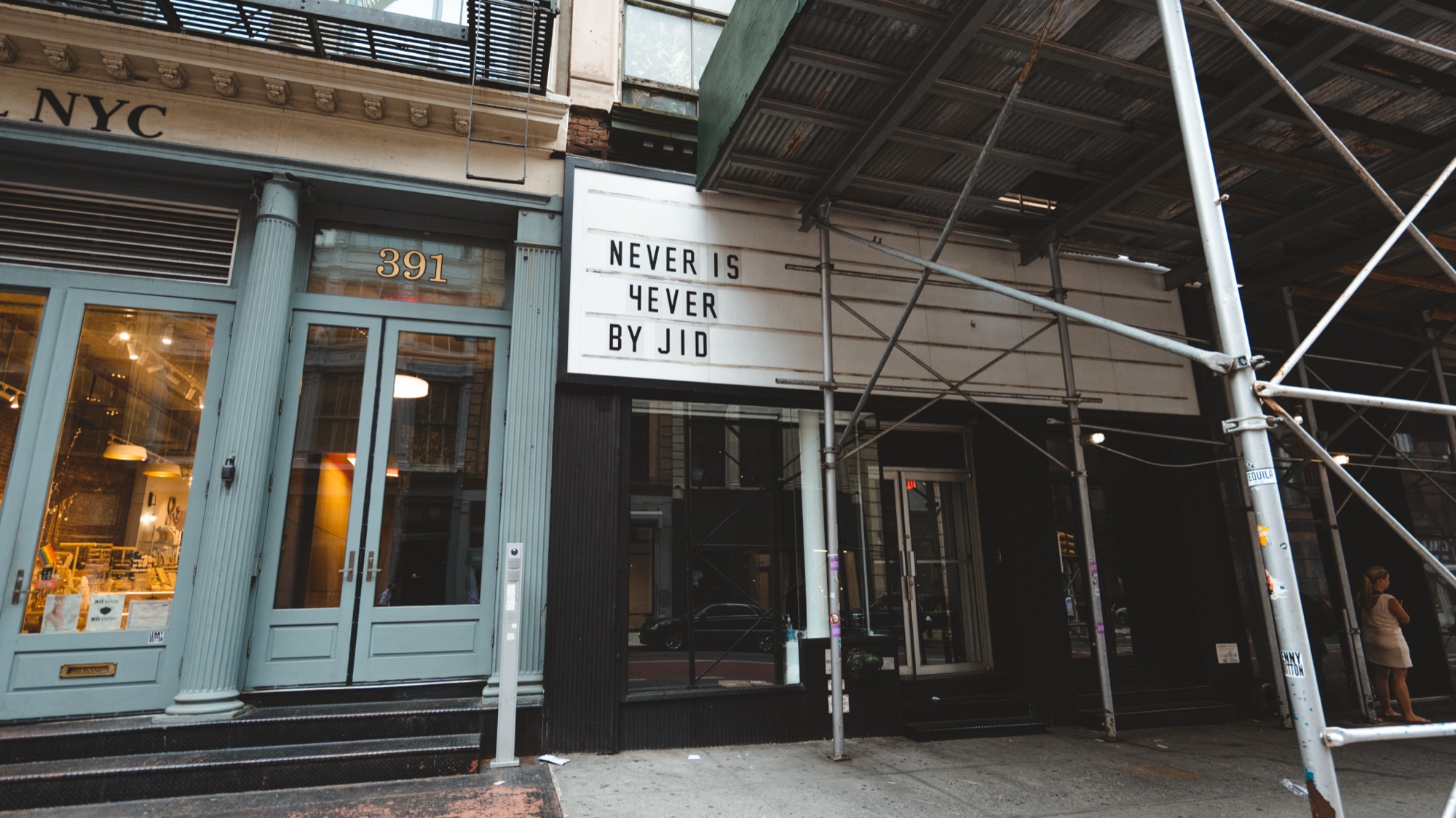 Marquee reading Never Is 4ever By JID over a doorway between green scaffolding and a NYC storefront