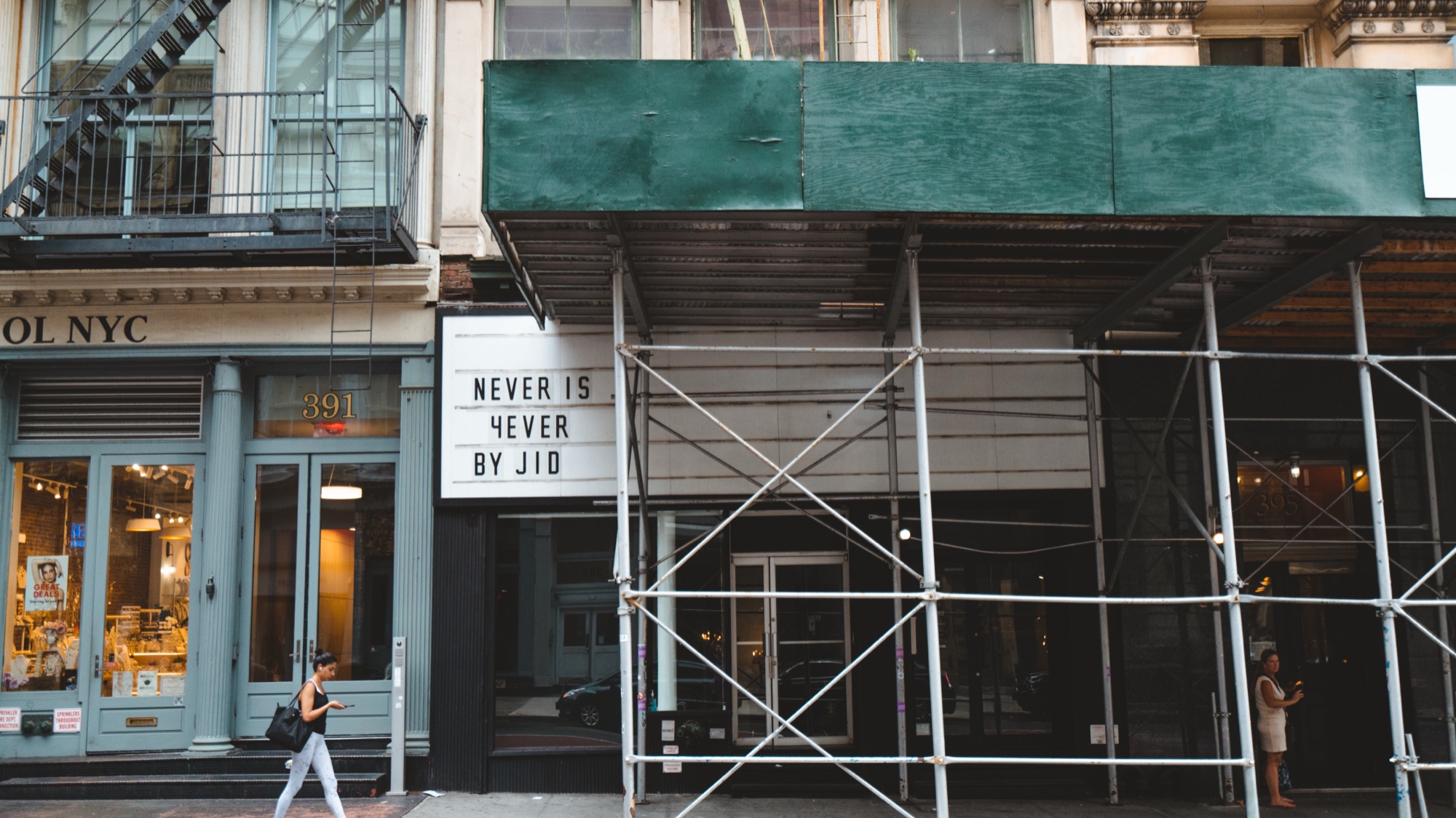 Marquee reading Never Is 4ever By JID beneath green scaffolding on a cast iron building facade