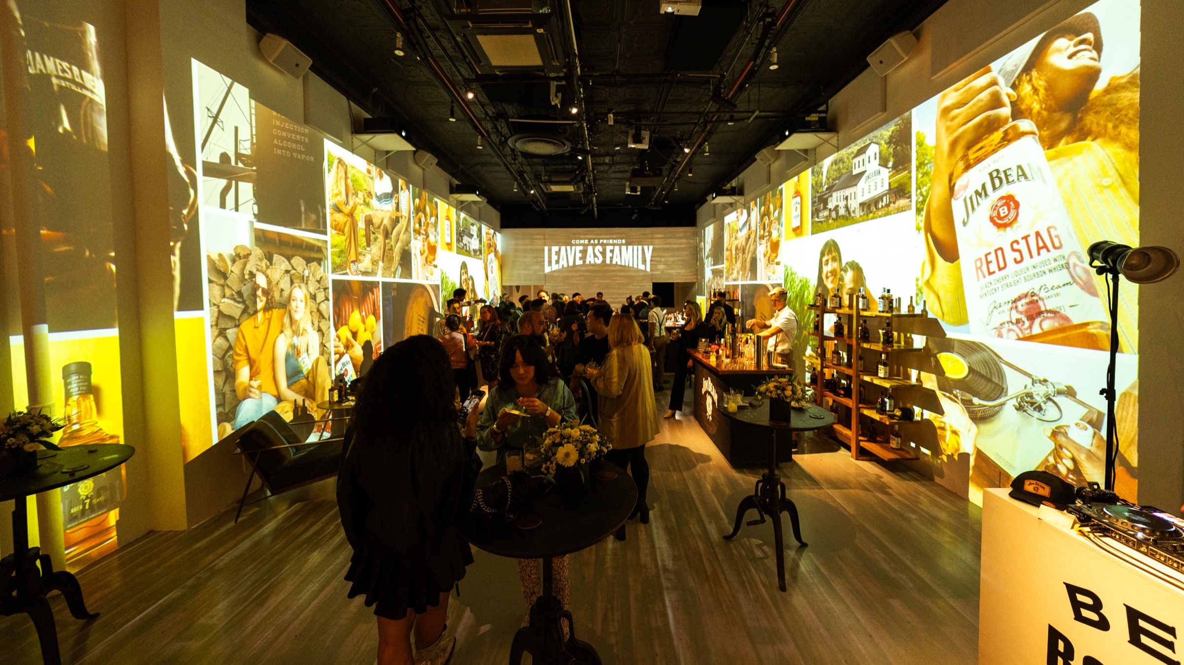 Guests gather around cocktail tables in a room whose walls are projected with Jim Beam Red Stag imagery
