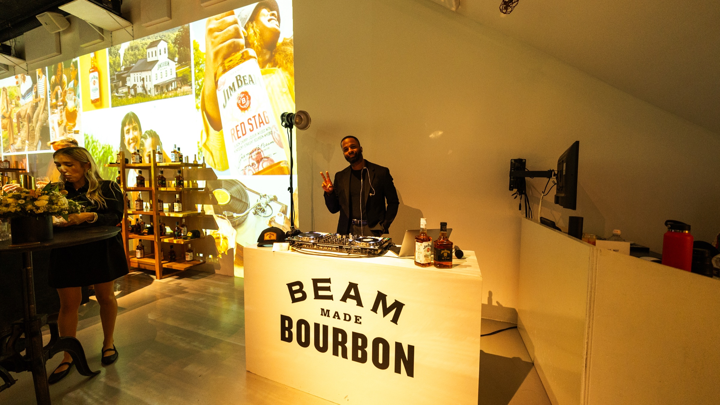 DJ behind a white booth reading Beam Made Bourbon with Jim Beam imagery projected on the wall