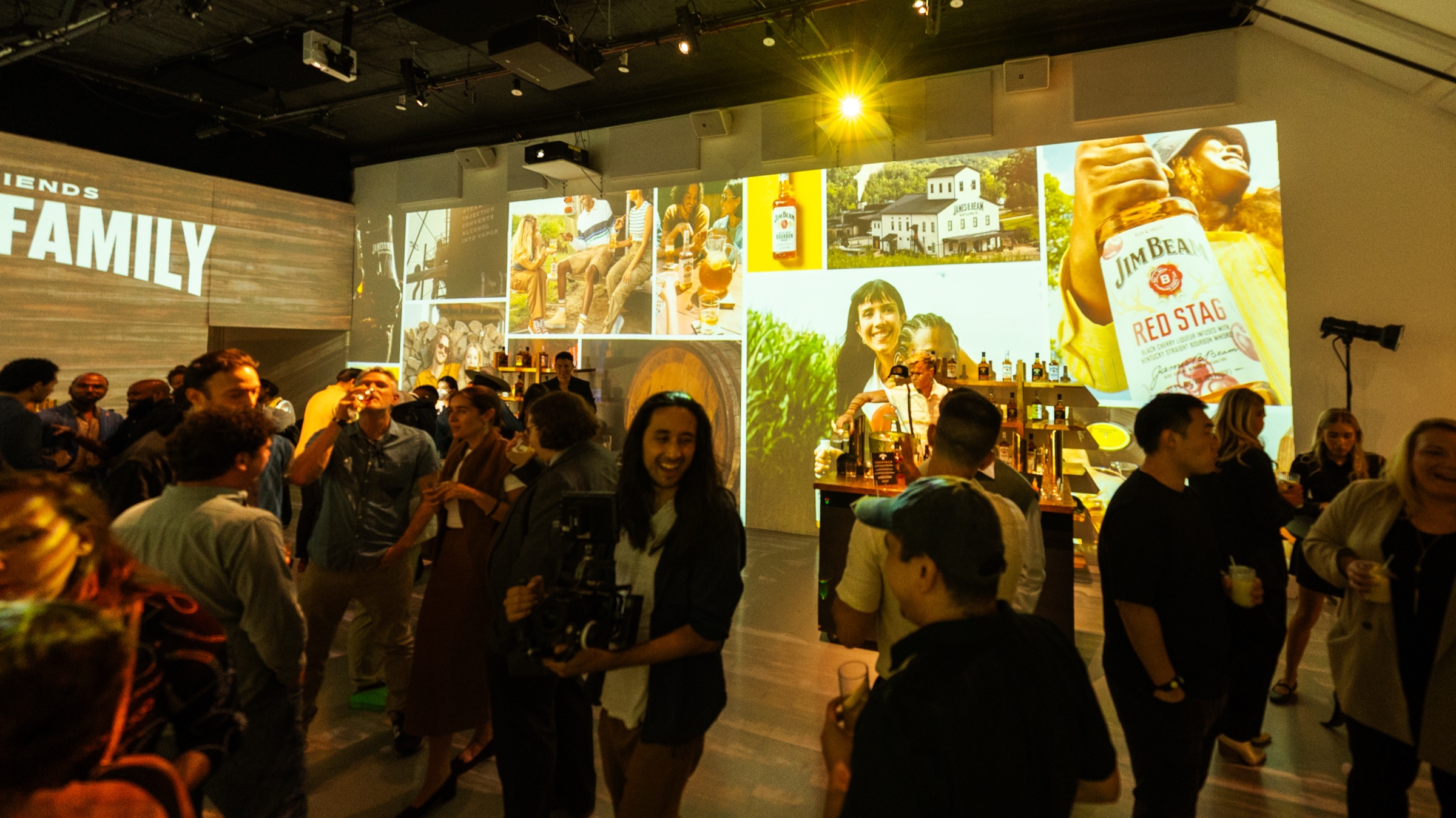 Crowd mingles beneath projected Jim Beam bottles and vintage photographs in a warmly lit event space