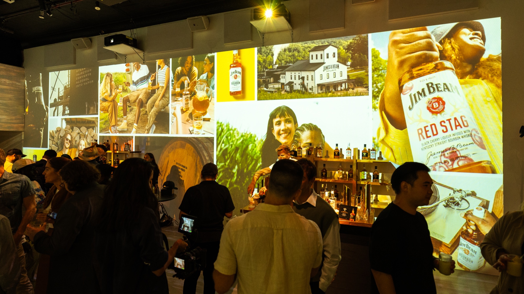 Guests gather below a wall of projected Jim Beam Red Stag imagery beside a lit shelf of bottles