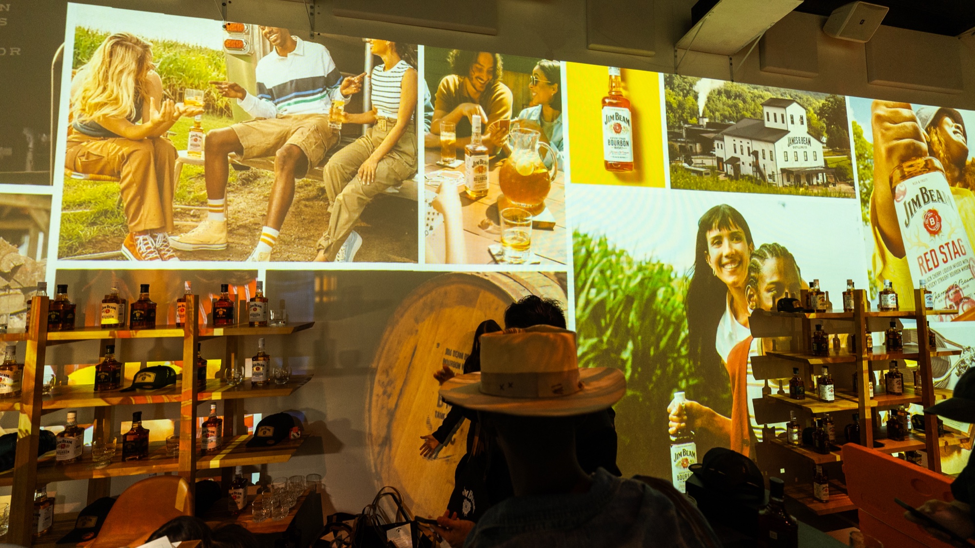 Man in a white hat at a bar under projected Jim Beam lifestyle photos and a barrel graphic