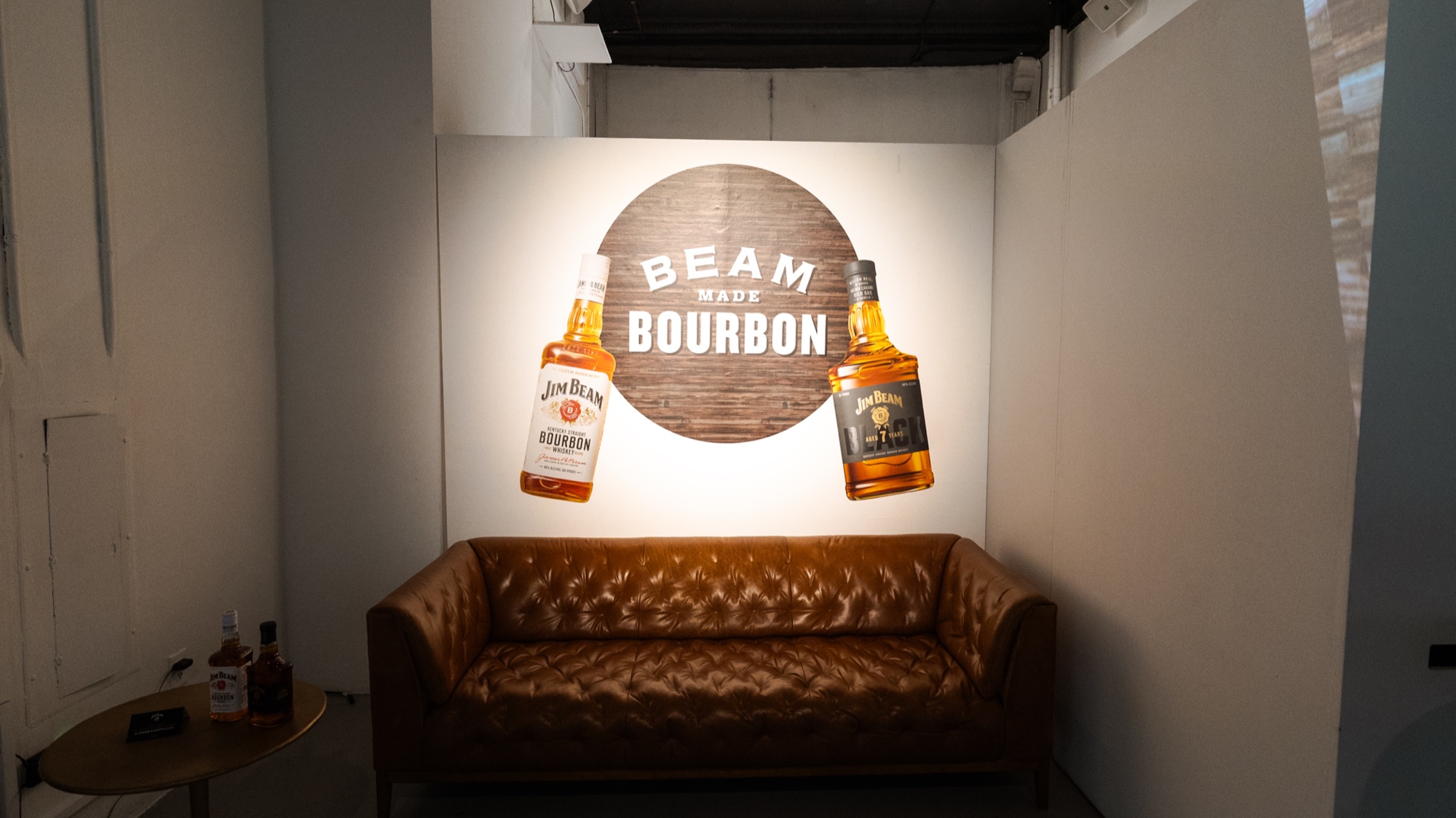 Tan tufted leather sofa beneath a Beam Made Bourbon wall graphic flanked by two bottle illustrations