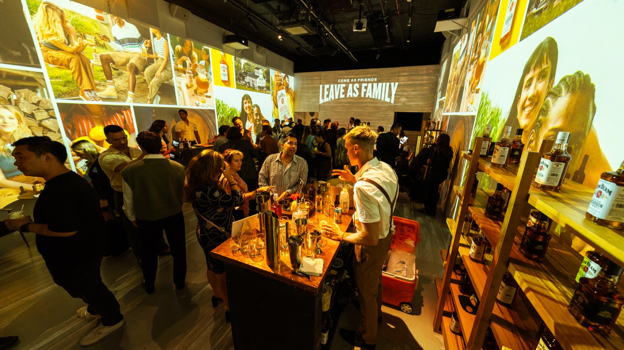 Bartender in a white shirt pours at a wooden bar as guests fill a room under Leave As Family signage