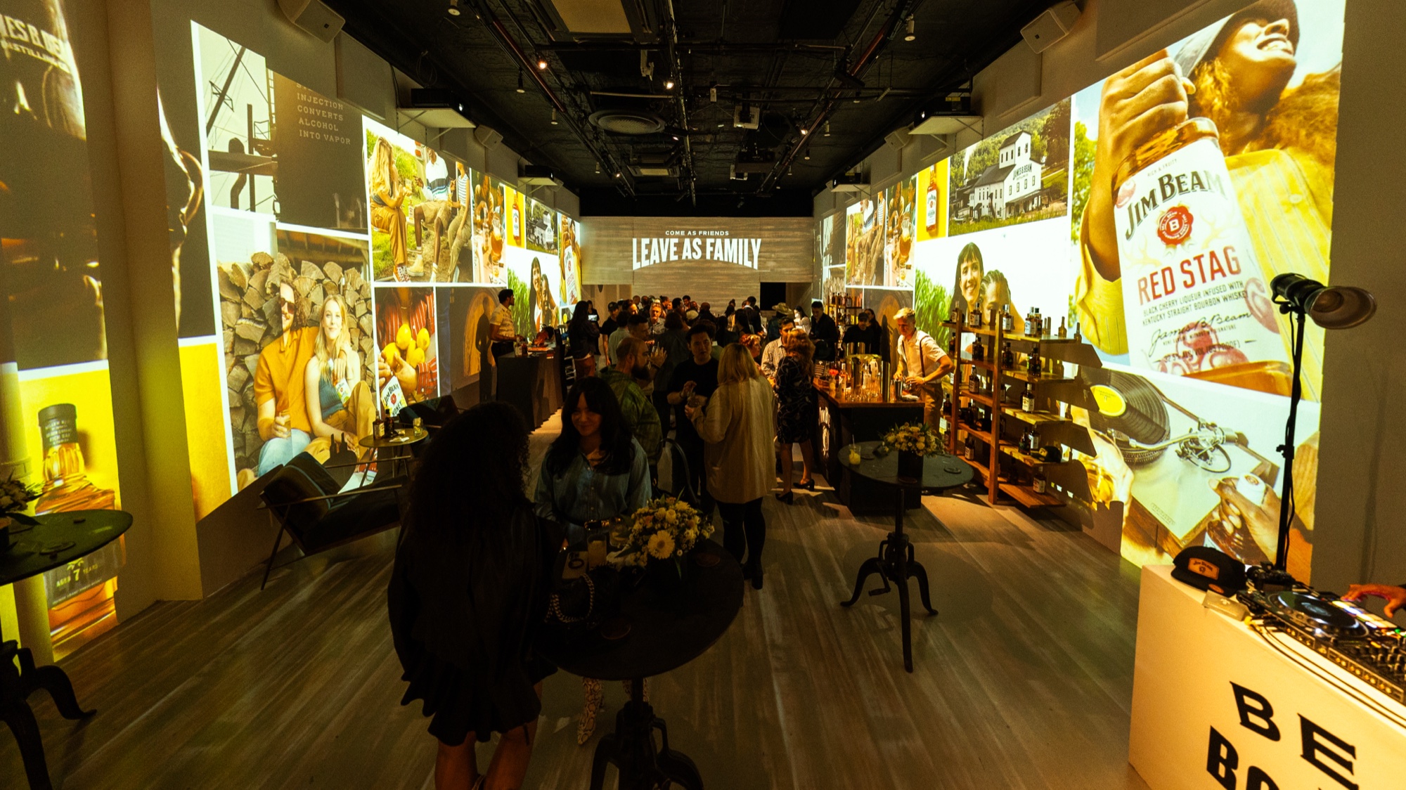 Long room lined with projected Jim Beam imagery, guests around cocktail tables and a Red Stag bottle graphic