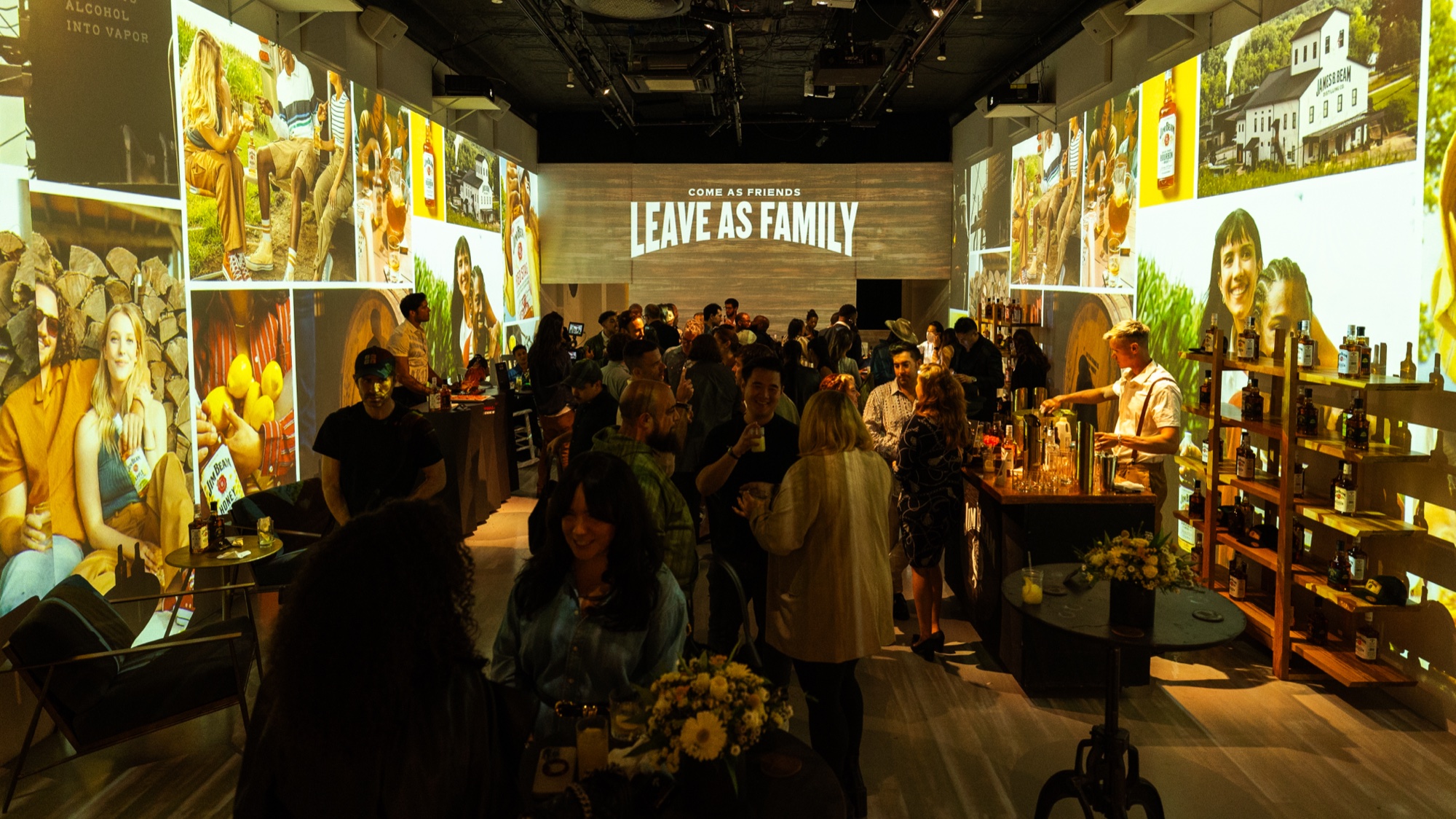 Wide view of a full room with projected family photographs and the words Leave As Family on the back wall