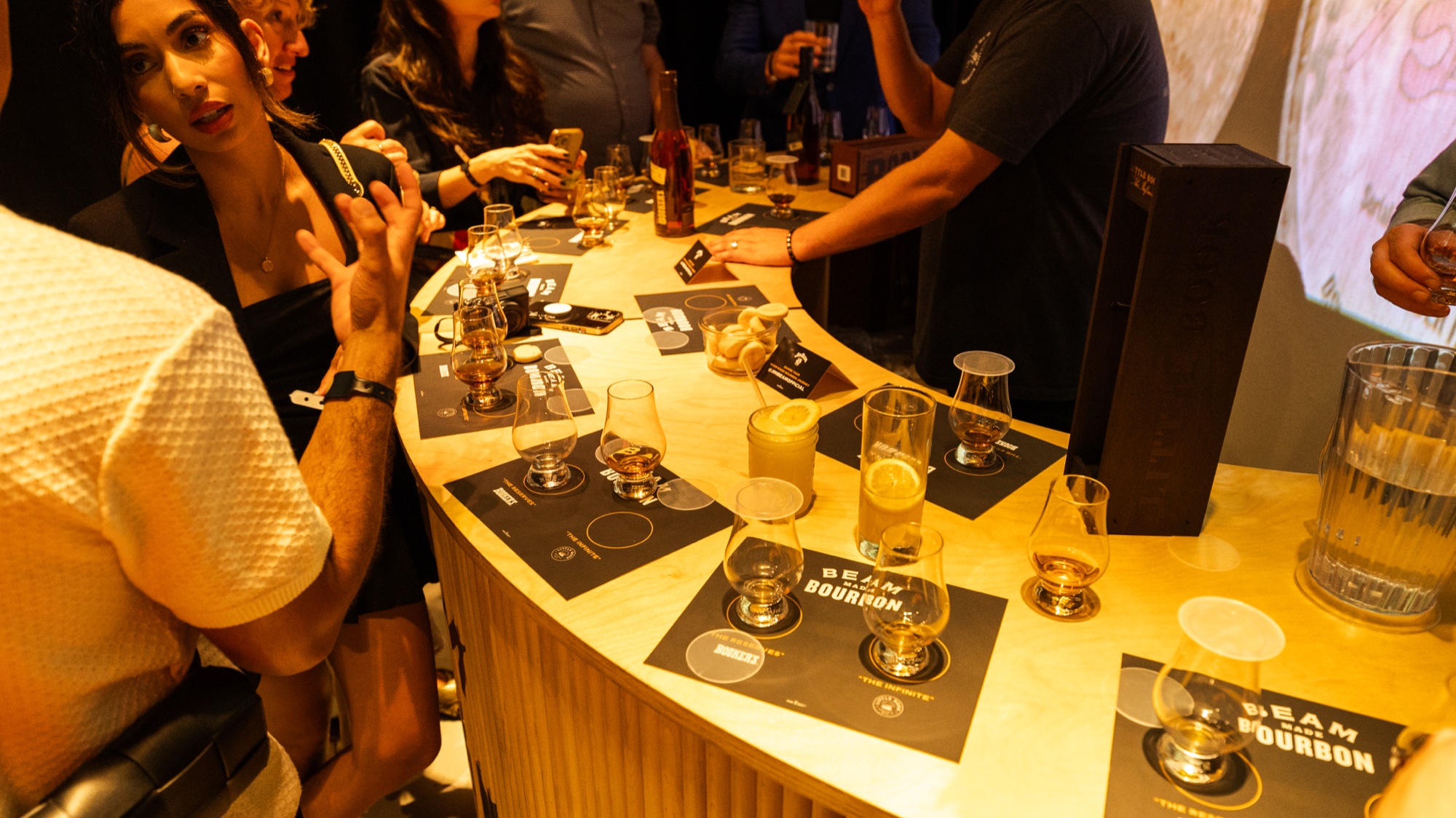 Curved bar top with Beam Made Bourbon tasting mats, glasses of whiskey and guests leaning in