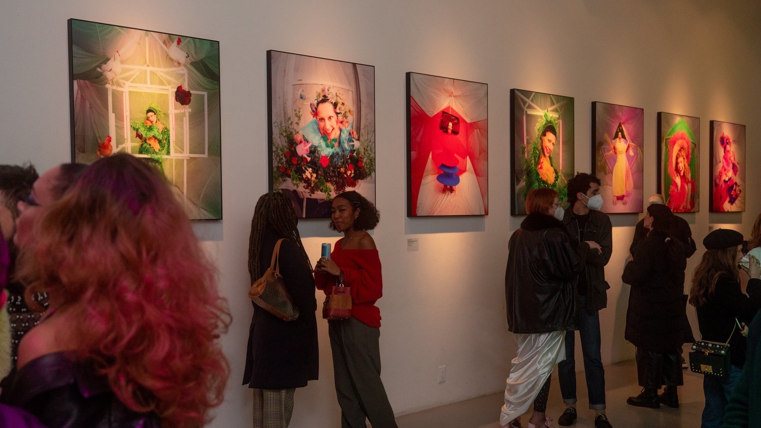 Guests in bold outfits admire a row of surreal floral portraits by Jordan Milligan