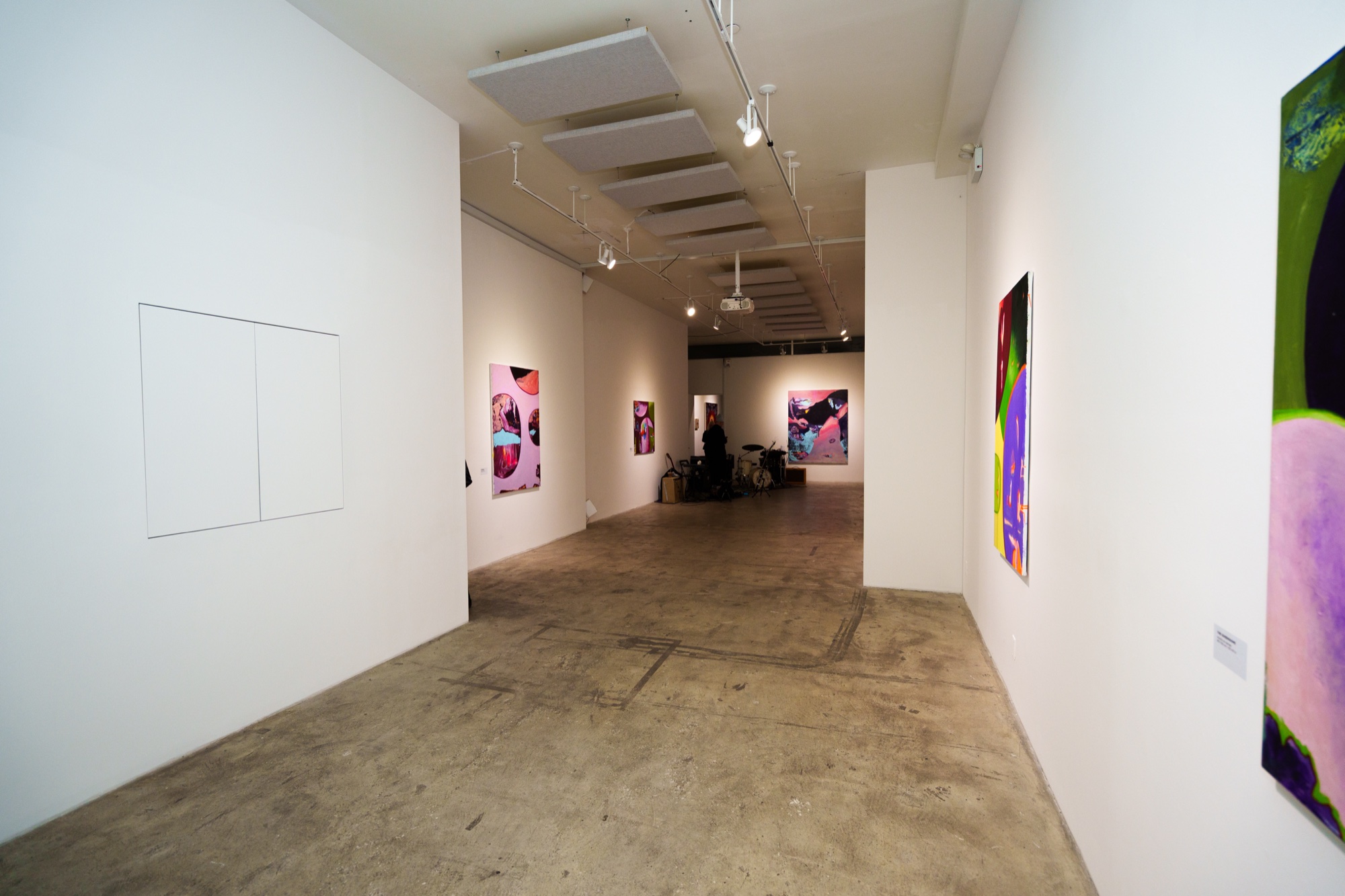 Long white gallery corridor with a concrete floor and bright pink and purple paintings on both walls