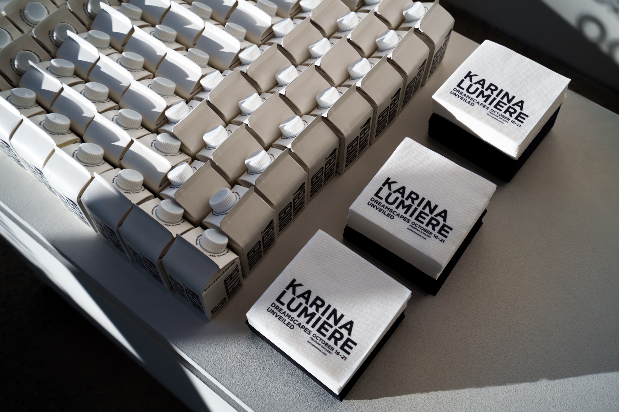 Rows of small white bottles and boxes printed with Karina Lumiere on a grey table in sunlight
