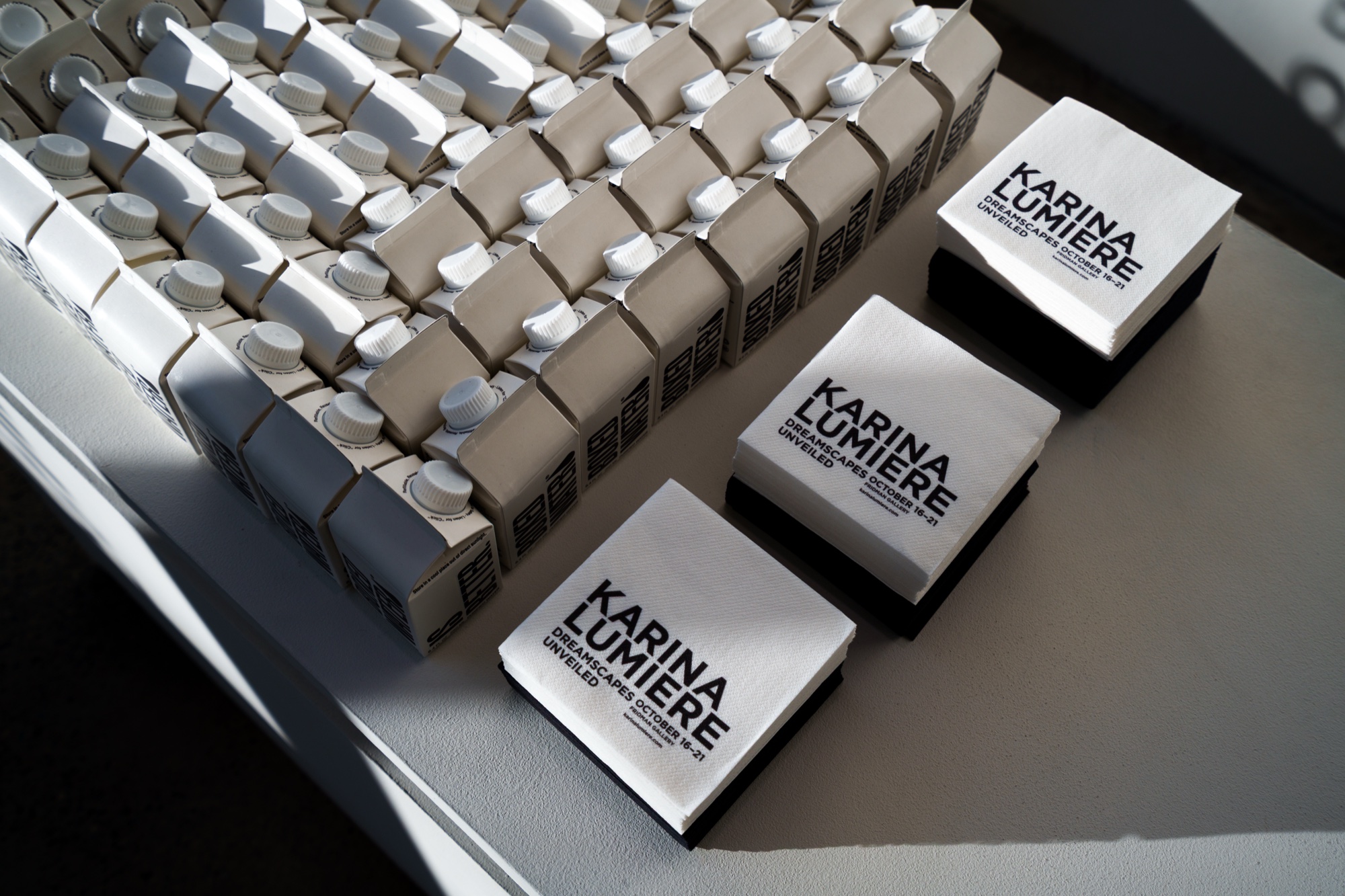 Stacked white boxes and tote bags printed with the name Karina Lumiere on a sunlit white table