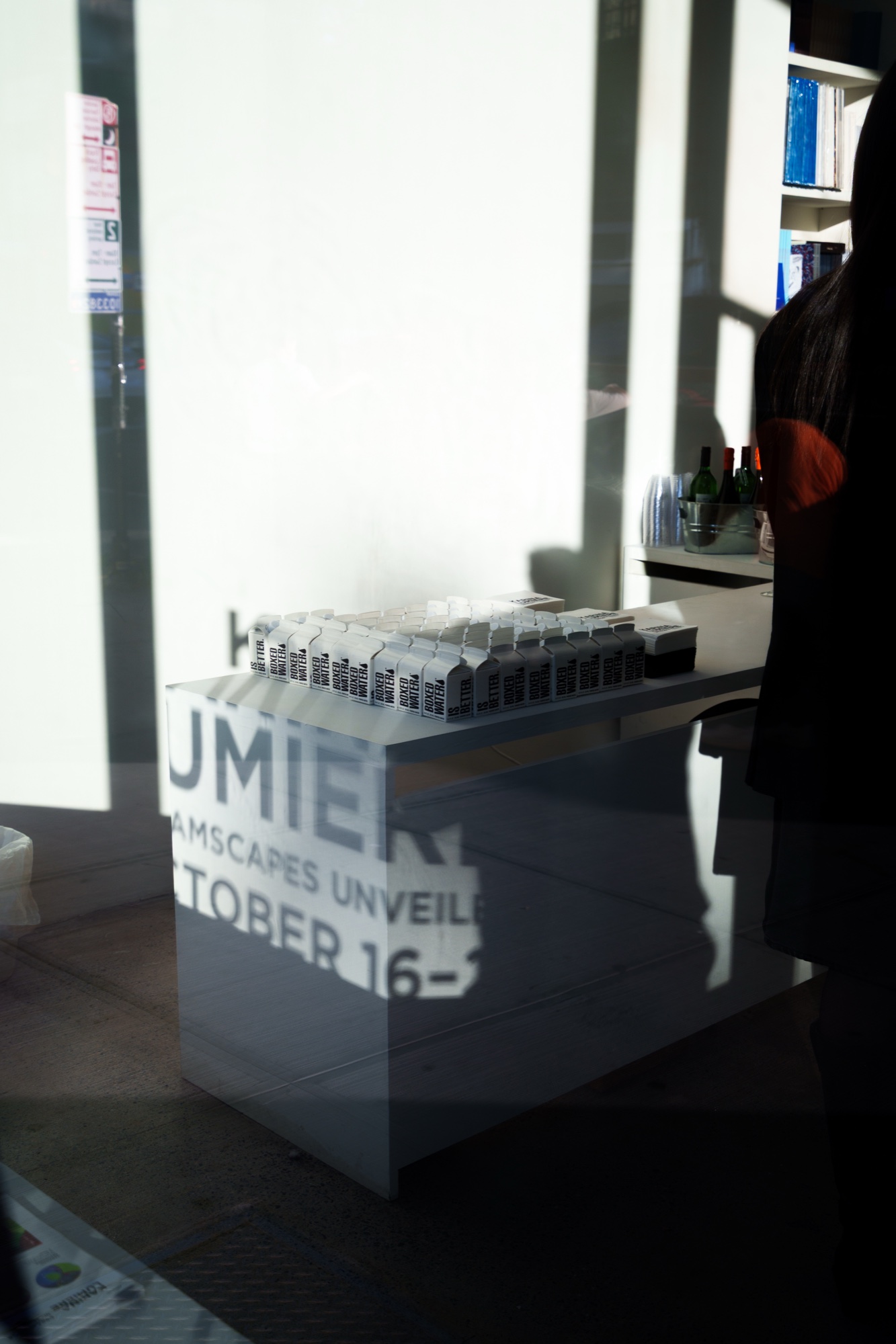 View through a shop window of a table of small white boxes, Karina Lumiere lettering and shadows on the wall
