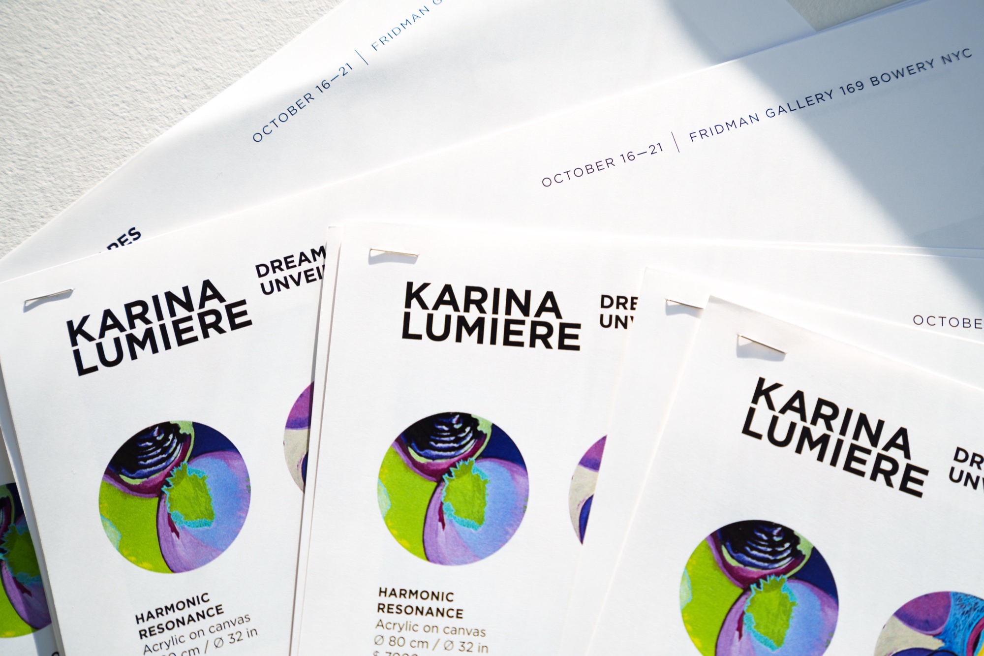 Stacked Karina Lumiere exhibition flyers show a round purple and green painting titled Harmonic Resonance