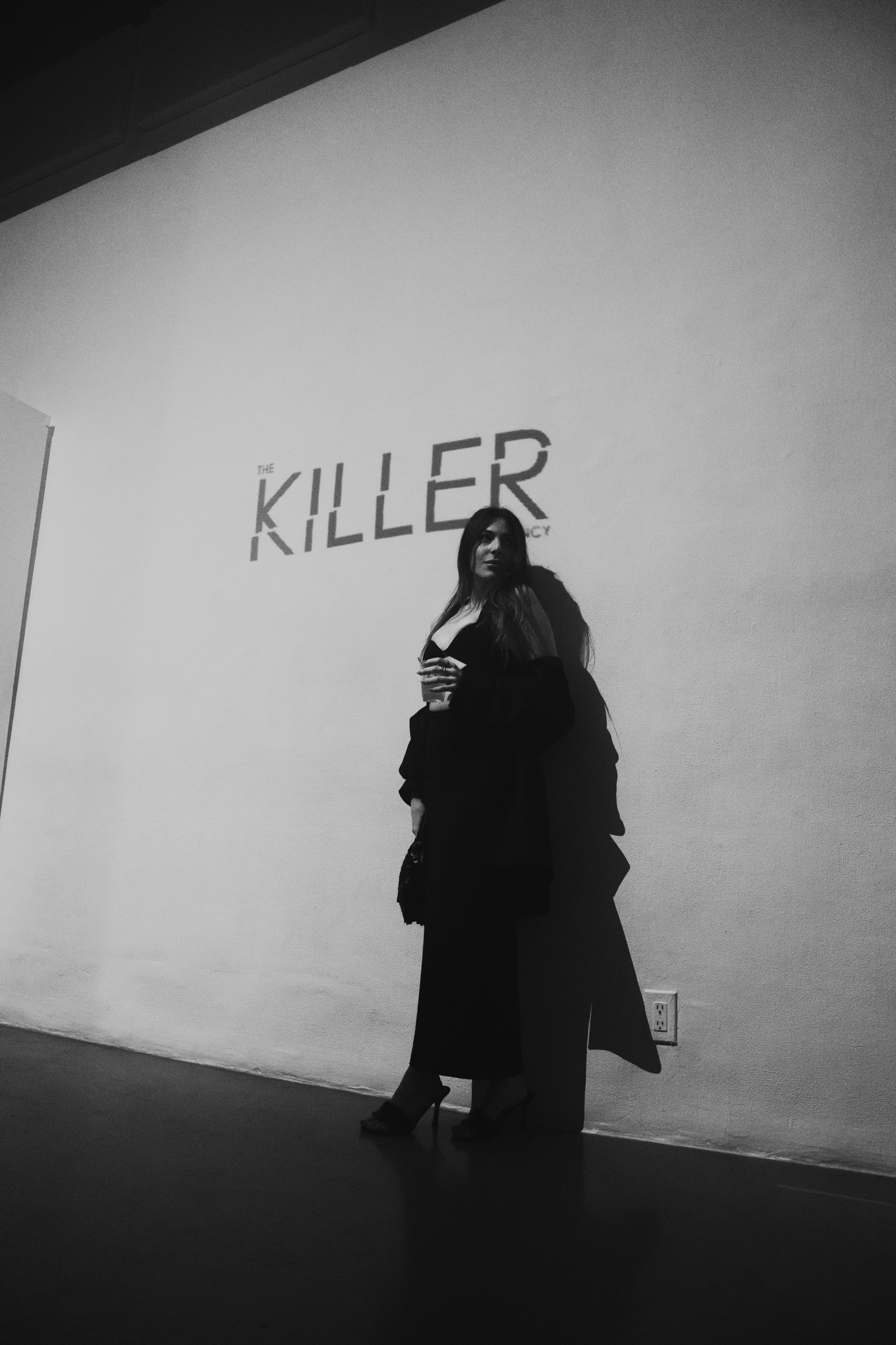 Black and white portrait of a woman in a long dress beside the projected Killer Agency logo