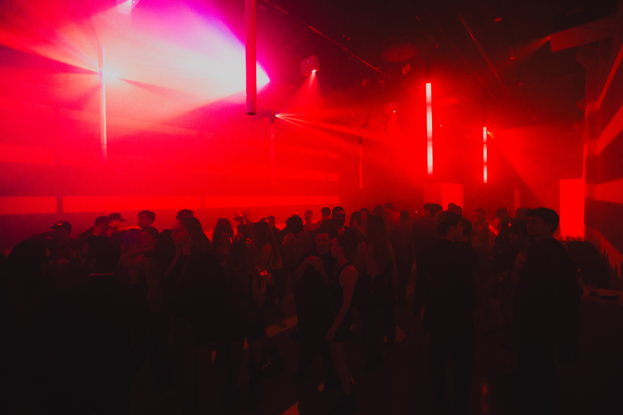 Silhouettes of dancers under red and pink beams of light cutting through haze in a dark club