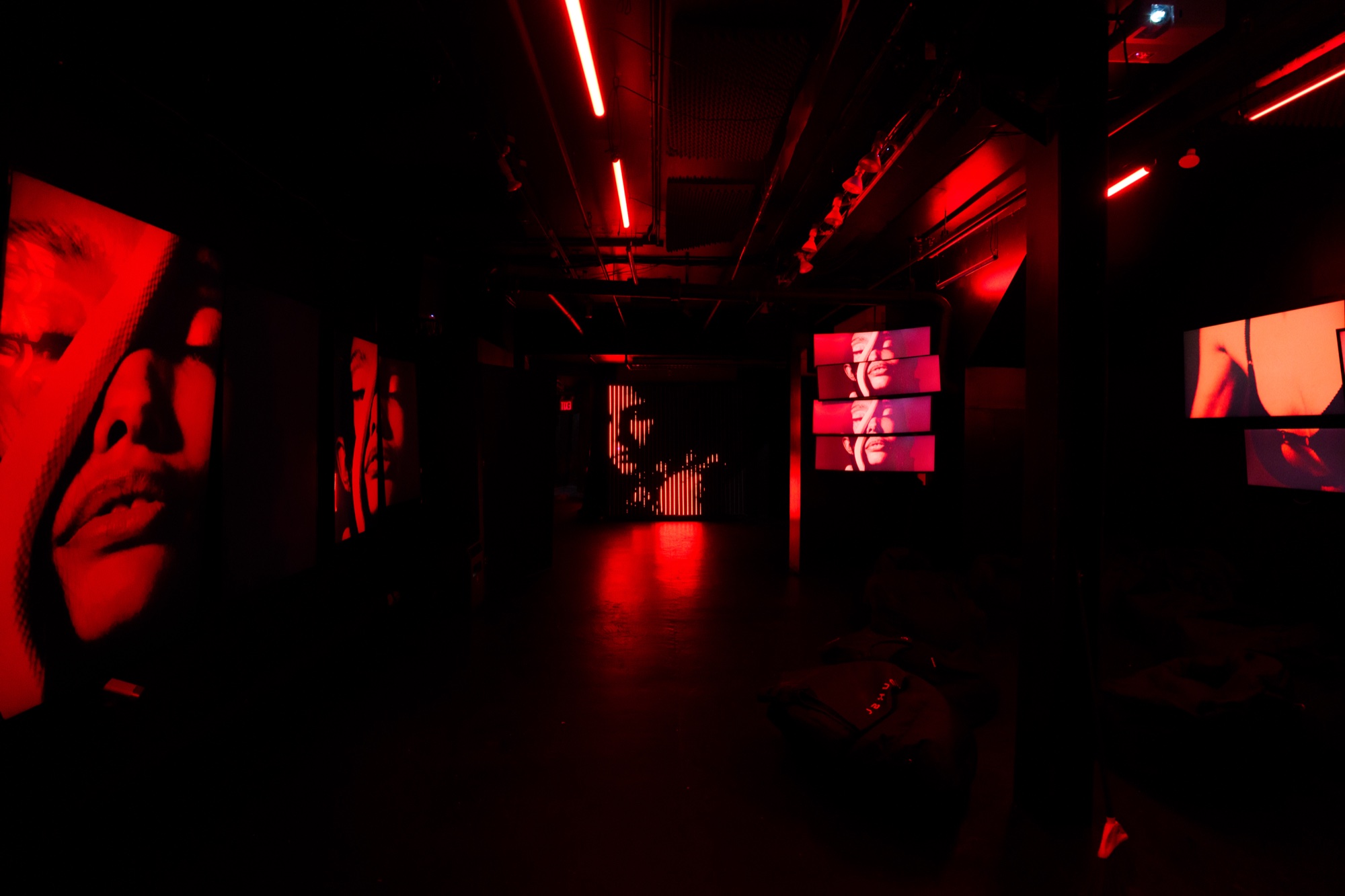 Dark corridor lit red with large screens showing close up faces and film stills along both walls