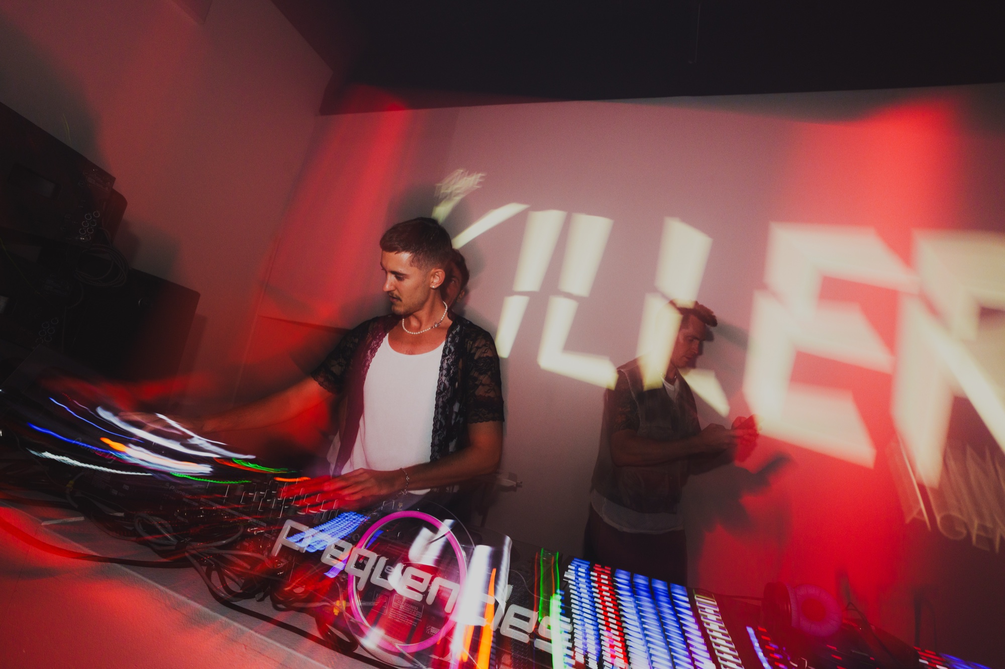 DJ mixes under a projected Killer logo and red light streaks at The Killer Agency party in NYC