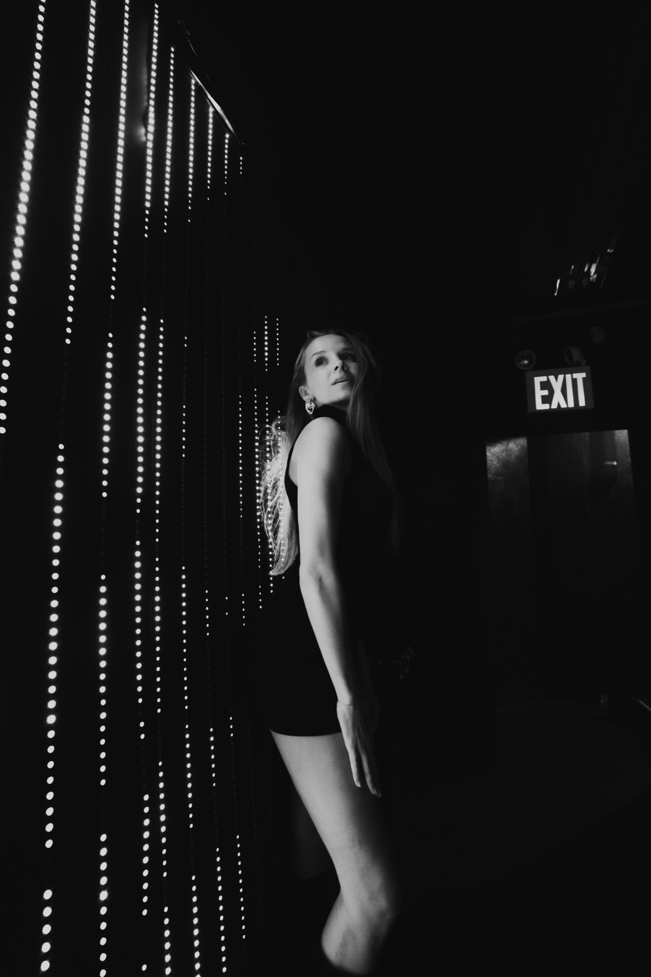 Black and white view of a woman in a black dress beside a curtain of string lights