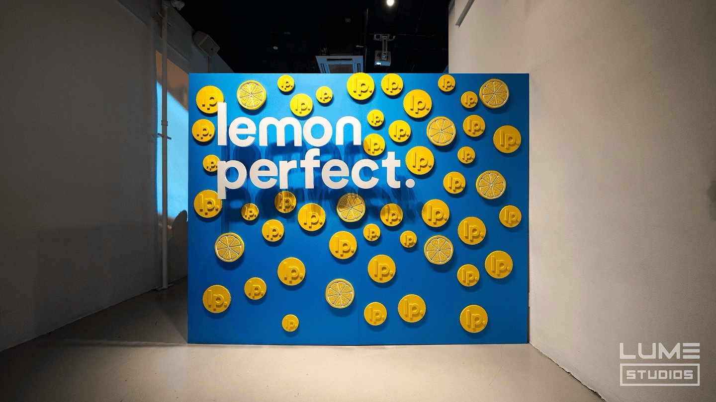 Blue photo wall covered in yellow Lemon Perfect coin props inside Lume Studios