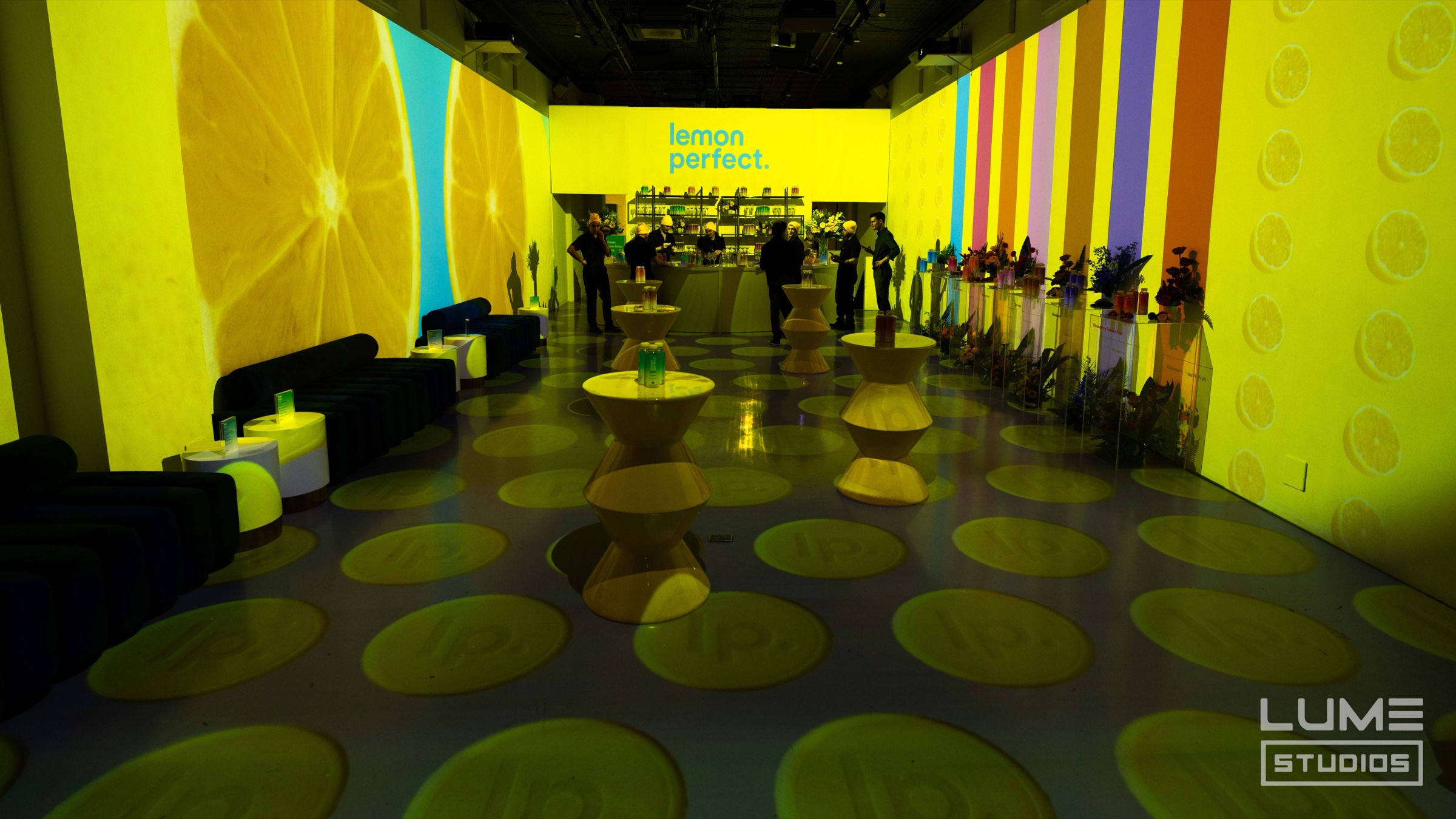 Lemon slice projections wrap a room of pedestal tables at the Lemon Perfect launch in Lume Studios