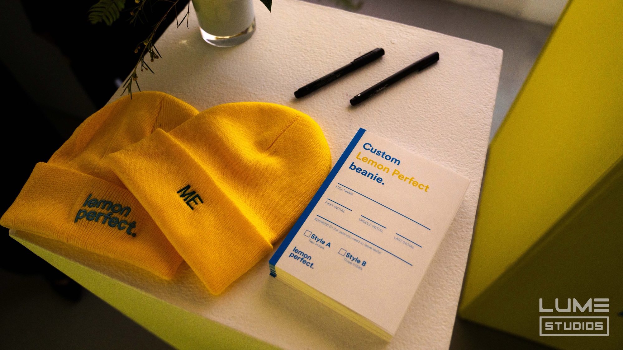 Yellow Lemon Perfect beanies with order cards and markers for custom embroidery on a white table