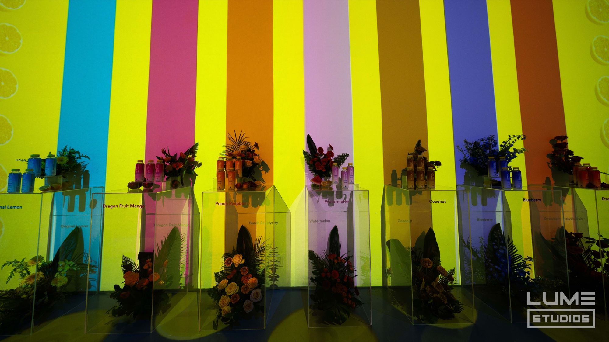 Row of Lemon Perfect flavor pedestals lit by rainbow stripe projections at Lume Studios