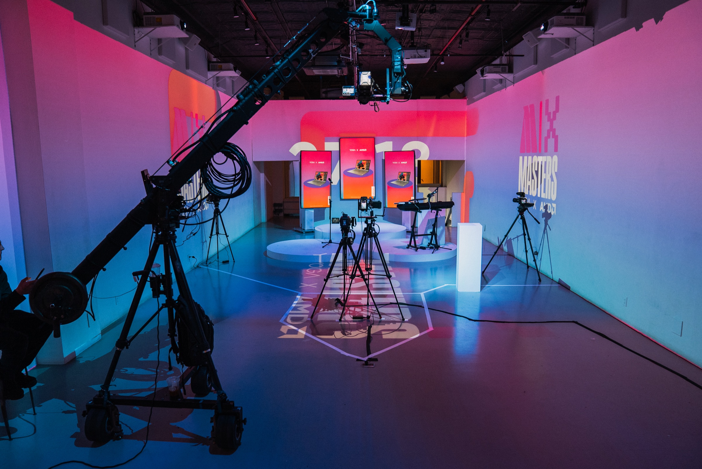 A camera crane and tripods face three glowing orange screens in a pink and blue studio with Mix Masters signage