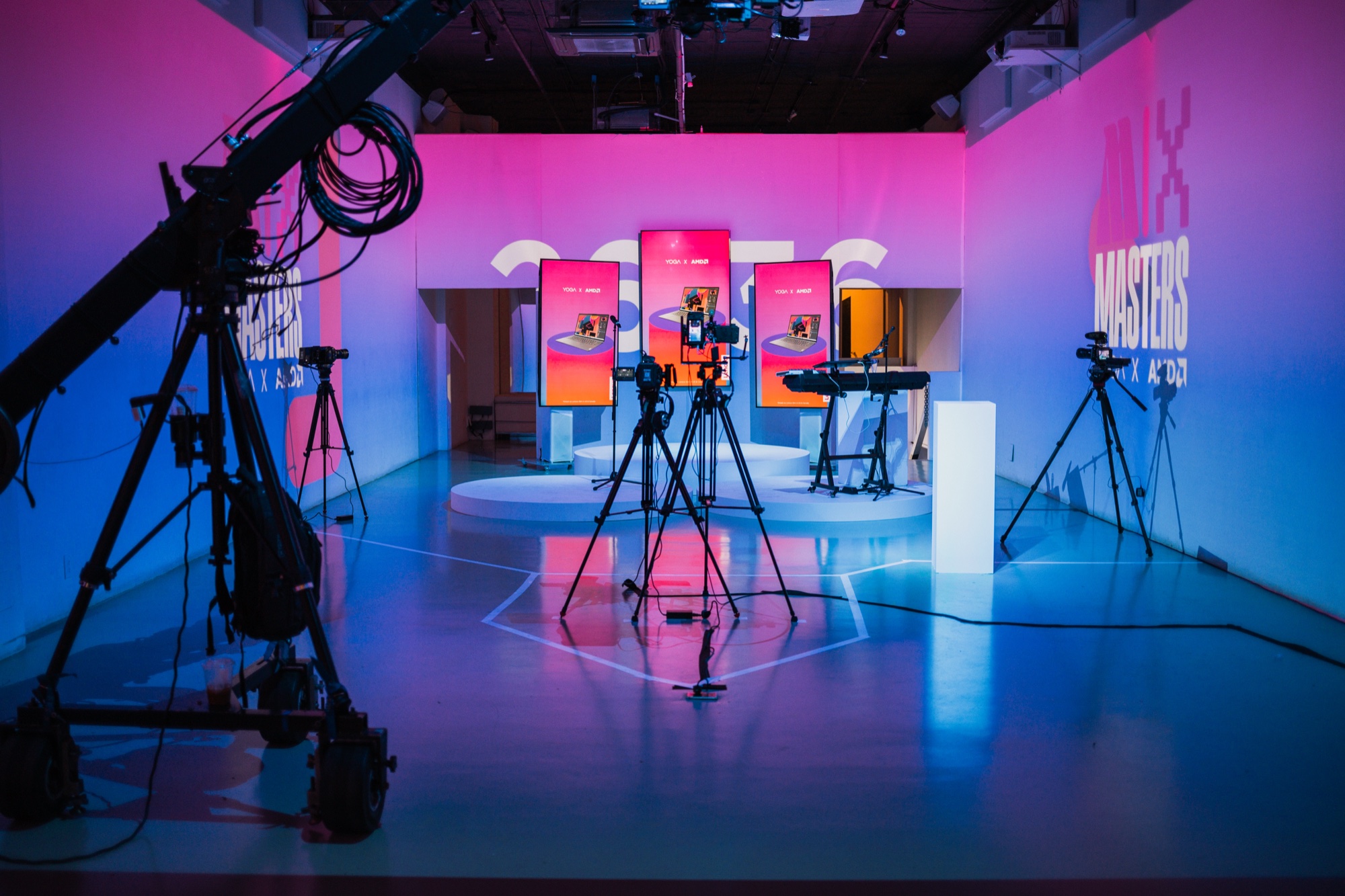 Tripod mounted cameras point at three orange lit screens on a round stage in a pink and blue studio