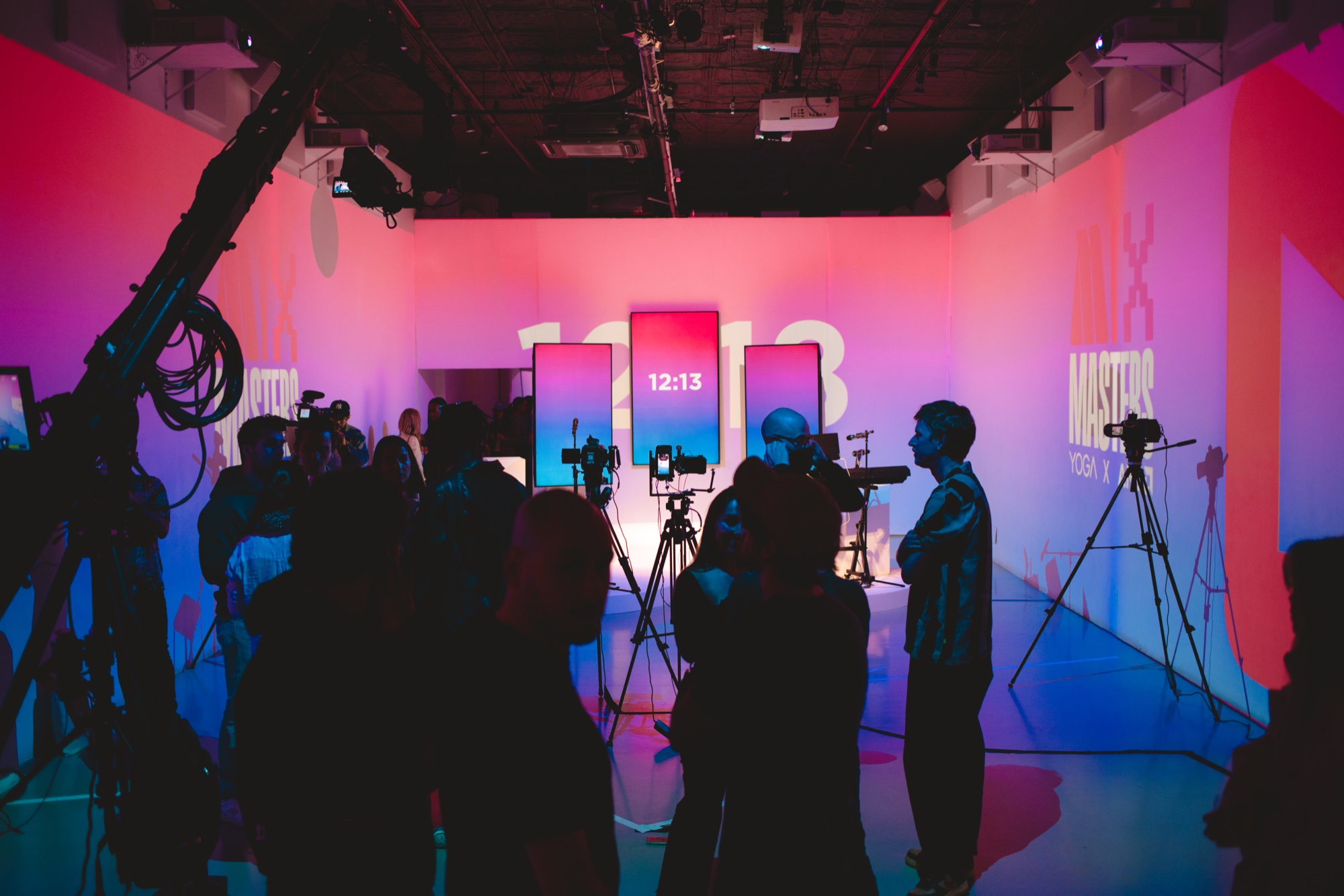 Silhouetted crew and camera rigs face three tall screens showing a countdown in a pink and blue lit studio