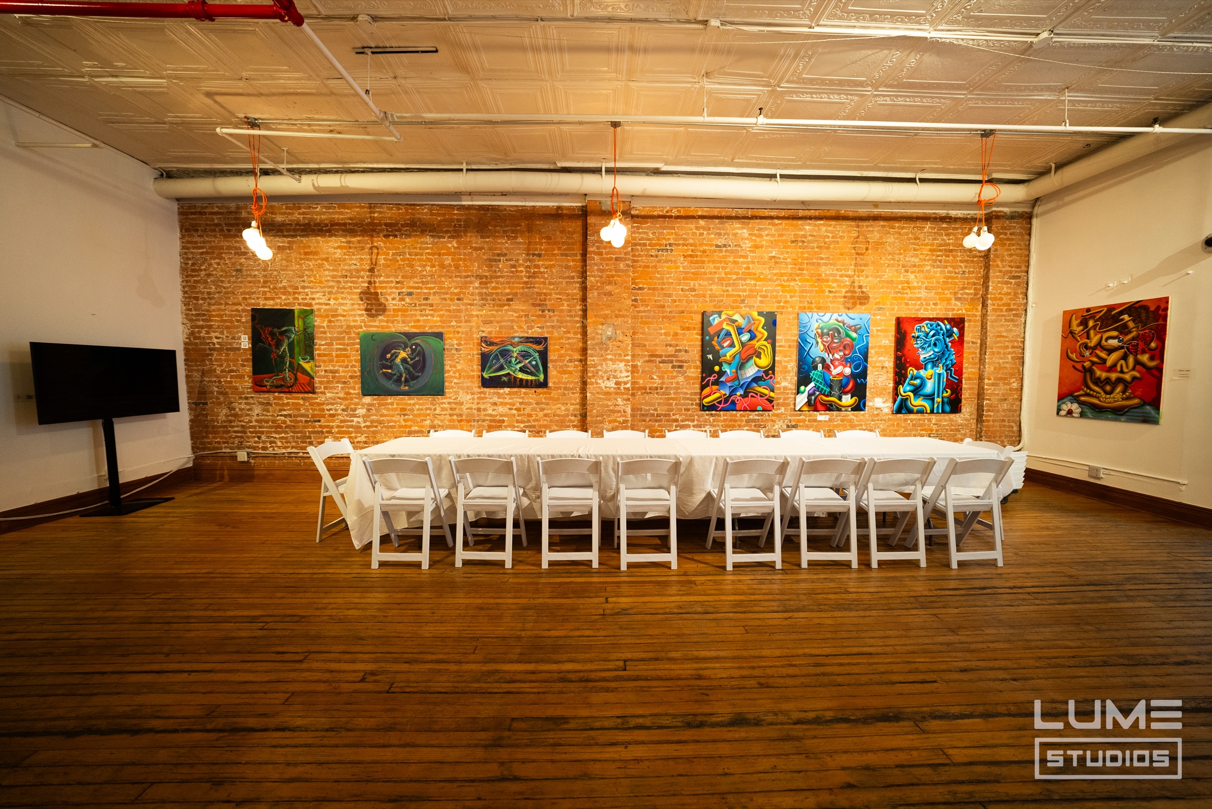 Long white banquet table with white folding chairs in a brick loft hung with colourful paintings