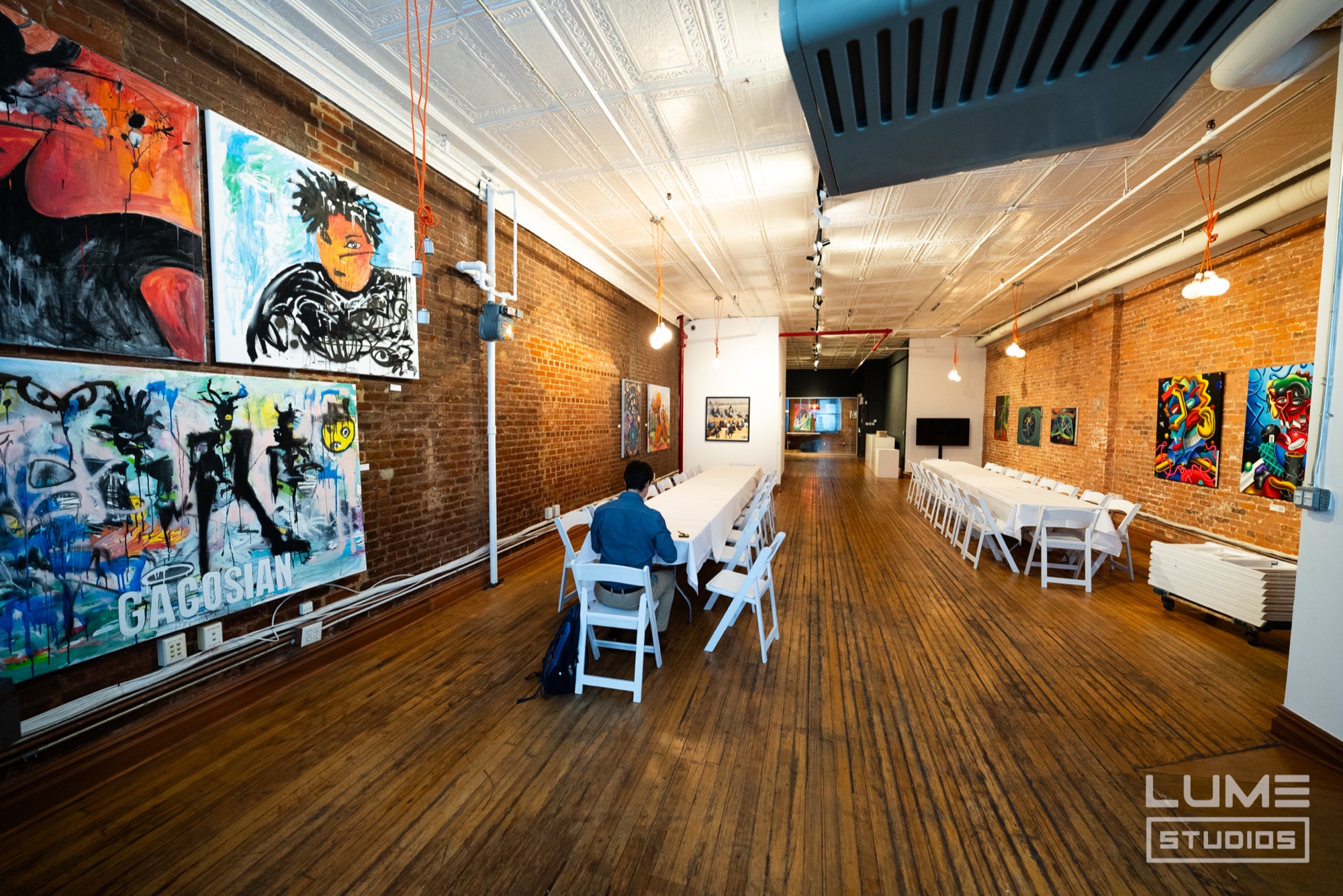 Guest seated alone at a long white table in a brick loft gallery lined with bold paintings