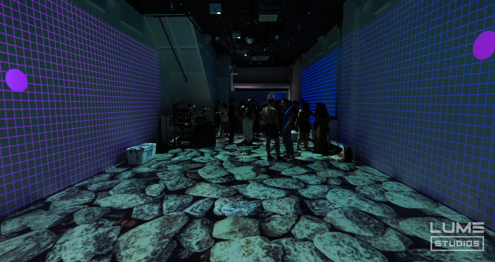 Guests stand at the end of a corridor whose floor is projected with grey boulders and walls with purple grids
