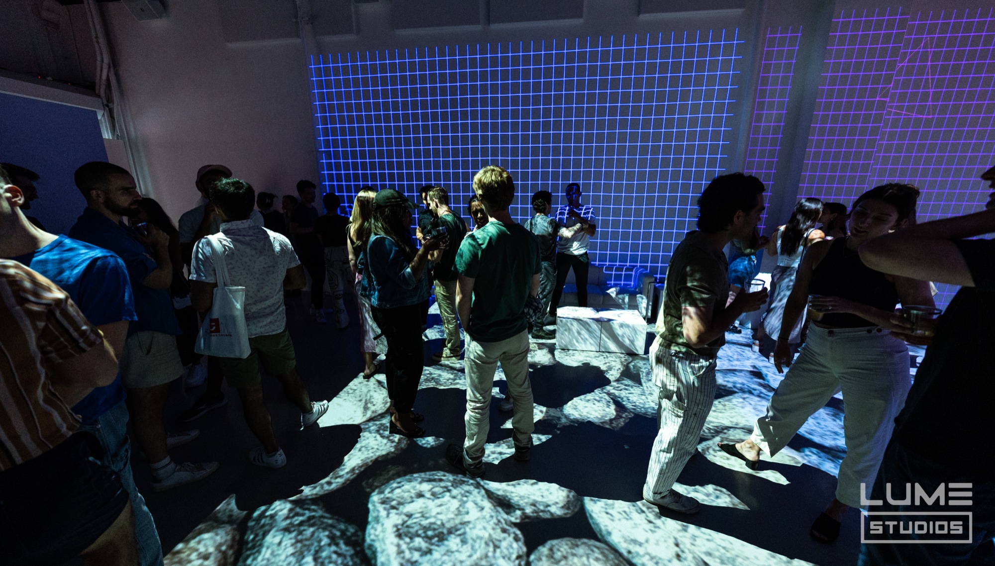 Guests mingle on a floor projected with grey boulders under a glowing blue grid wall