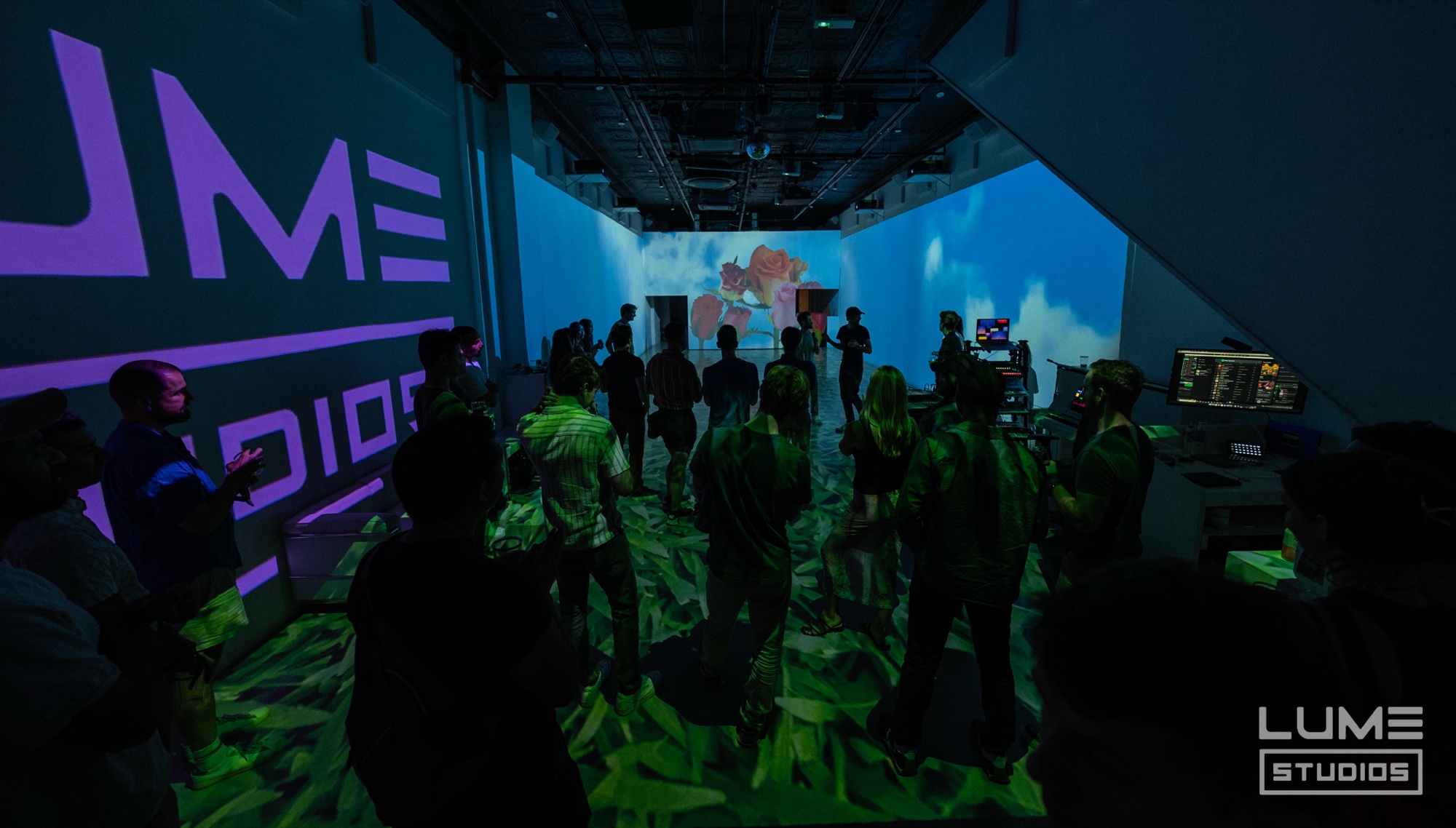 Crowd faces a wall projection at the end of a purple lit room with green shapes projected on the floor