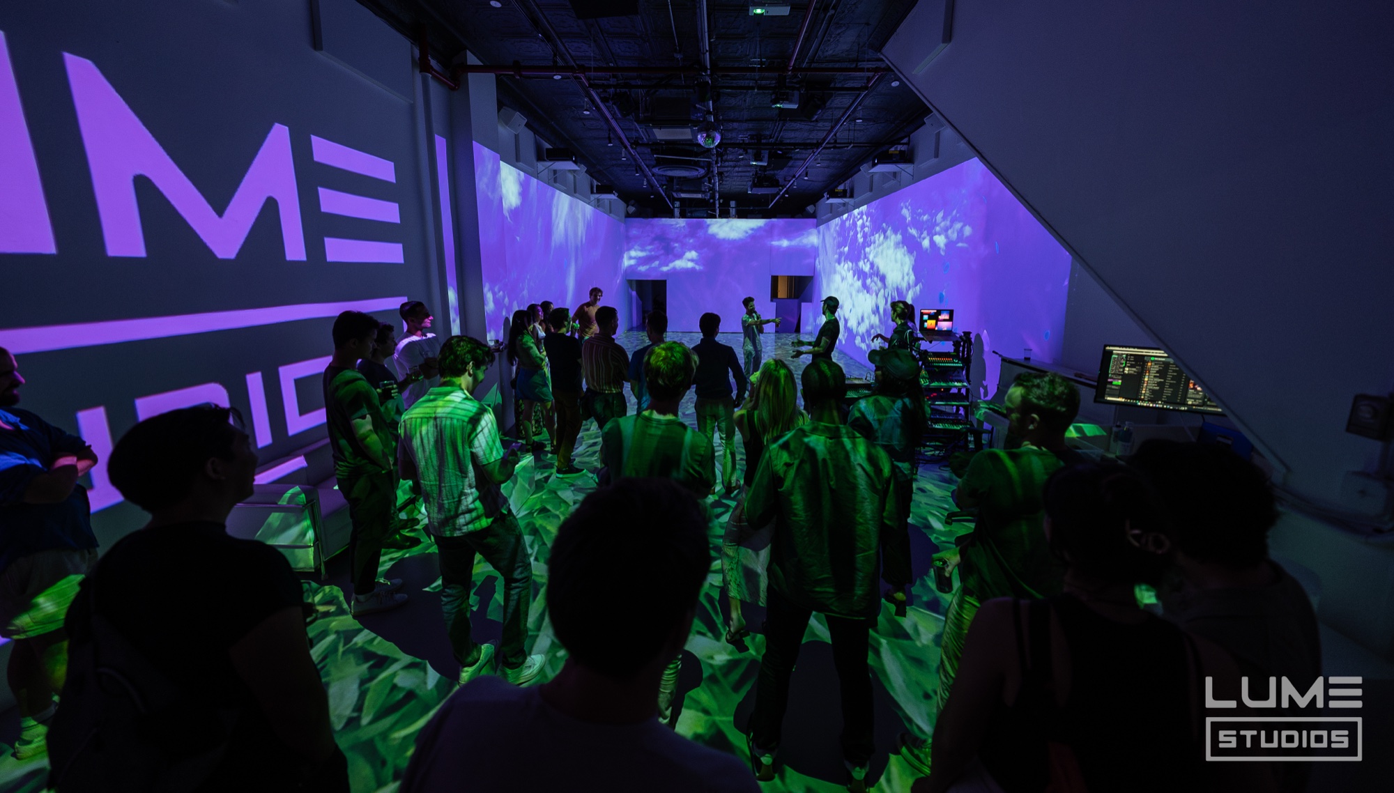 Guests dance under purple walls and green light on a floor of projected leaves beside a Lume logo