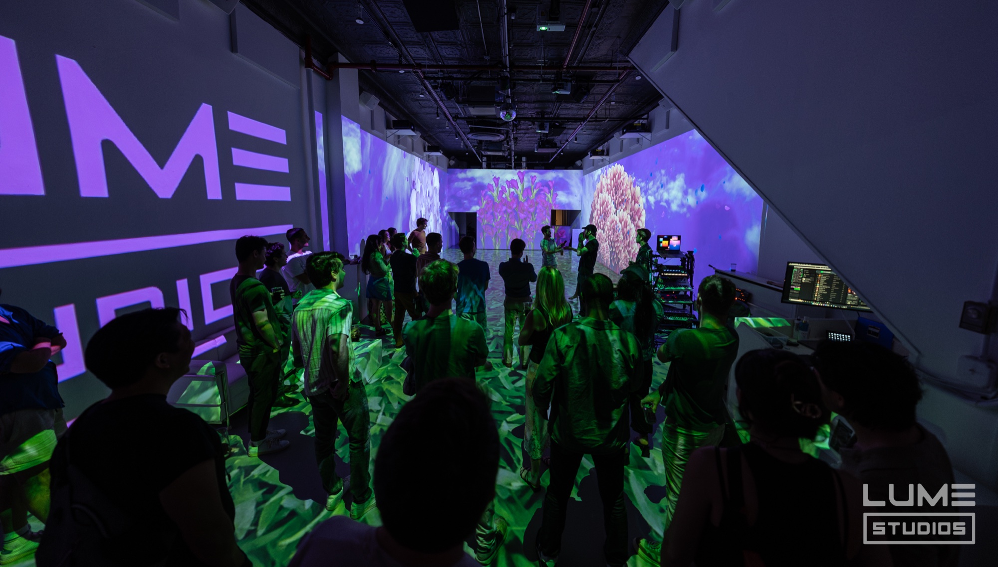 Crowd in green and purple light between a Lume logo wall and a pink coral projection